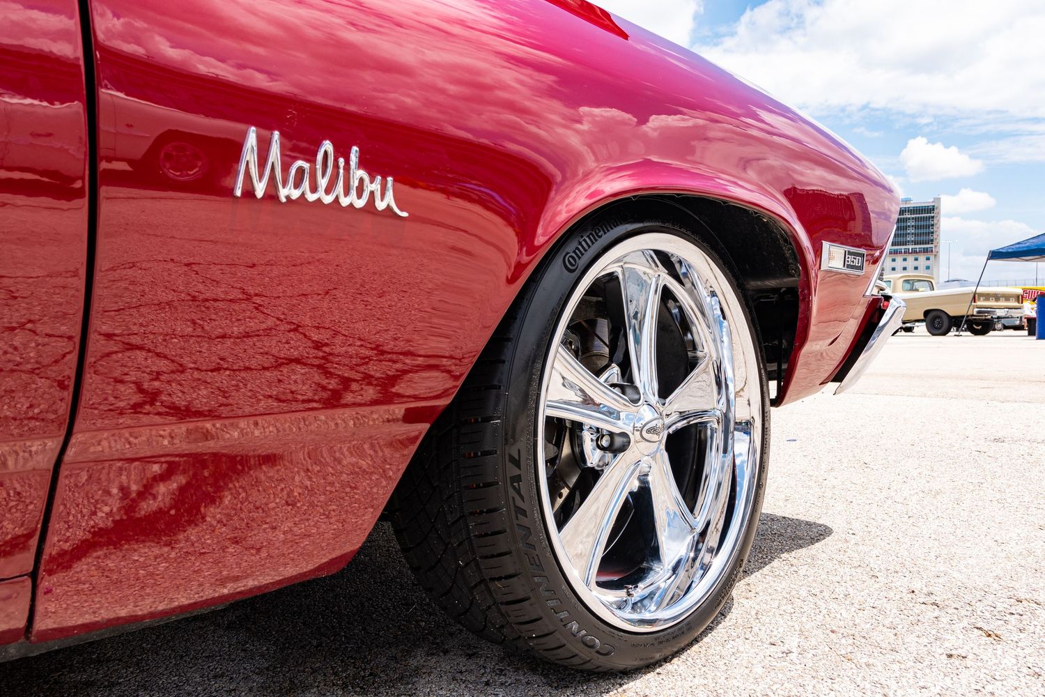 Close-up of a red Chevrolet Malibu classic car with chrome wheels on a sunny day.