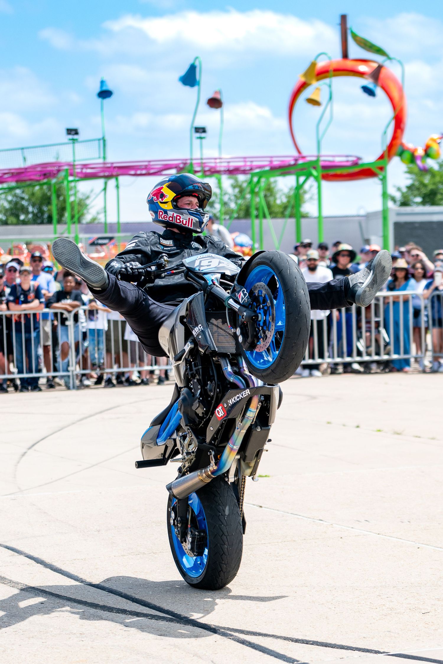 Motorcycle stunt rider performs wheelies and tricks in front of crowd at outdoor event.