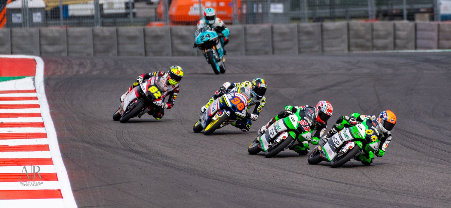 Multiple motorcycles race through a challenging corner section on a motorsport track.