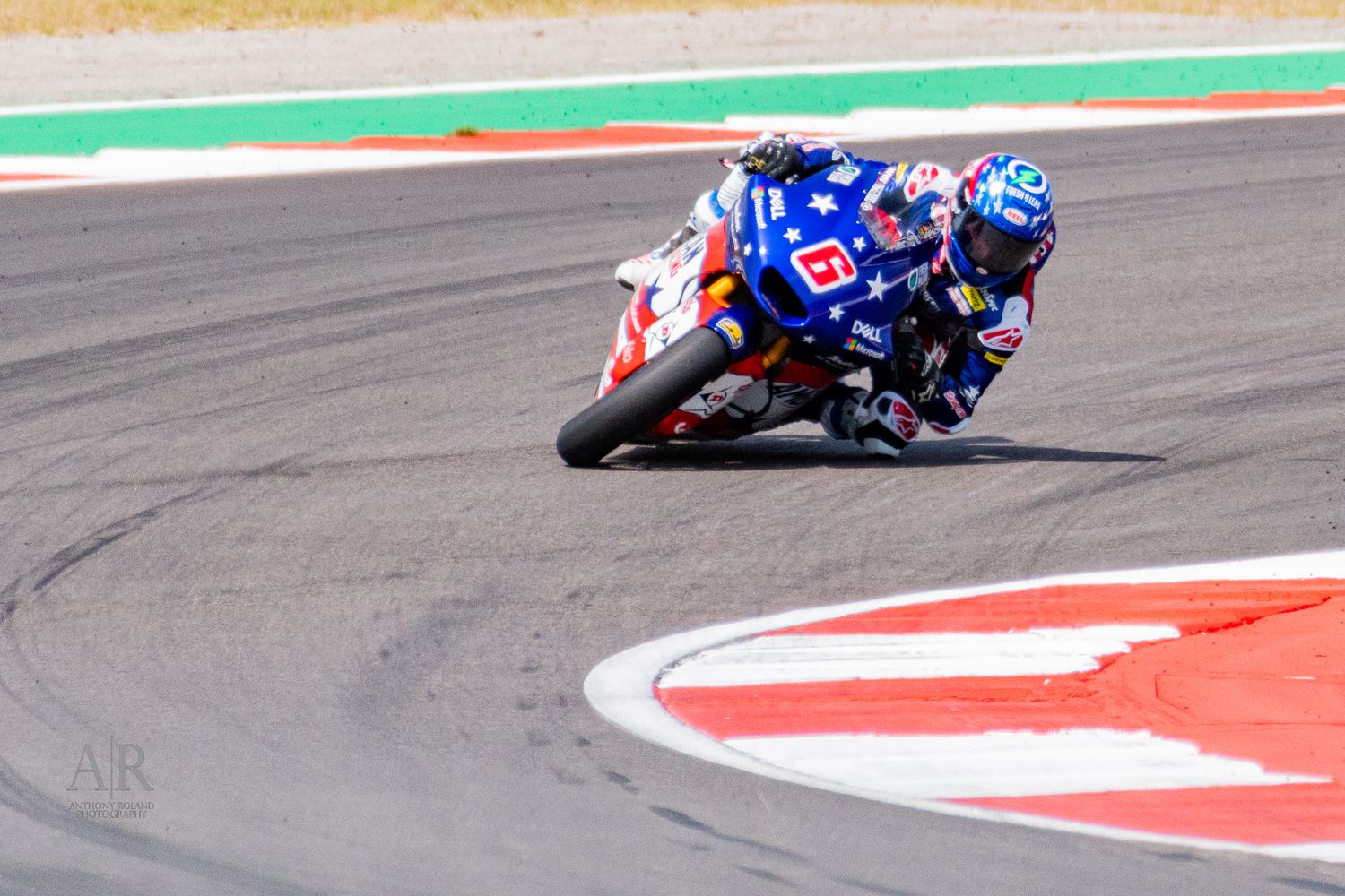 Racing motorcycle takes a sharp turn on a red and white curbed race track.