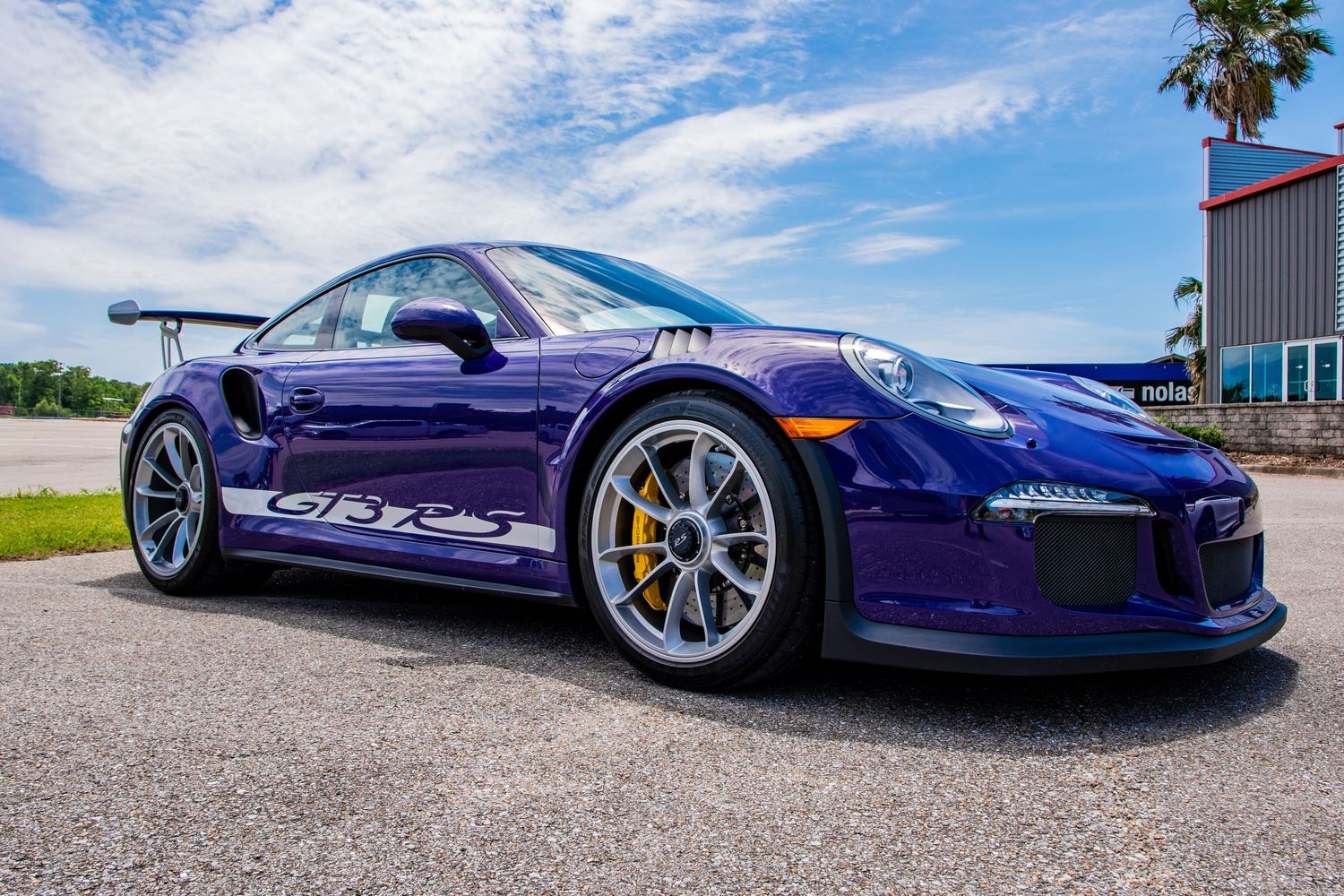 Purple Porsche 911 GT3 RS sports car parked outdoors with large rear wing and gold wheels.