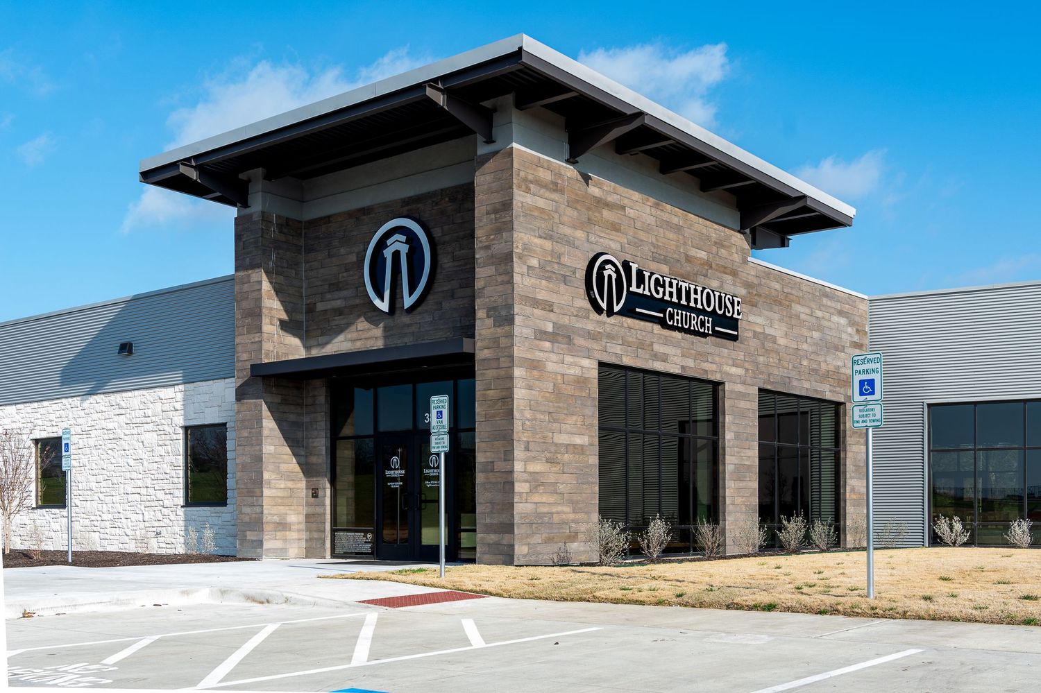 Modern commercial building exterior with stone facade and glass windows under blue sky.