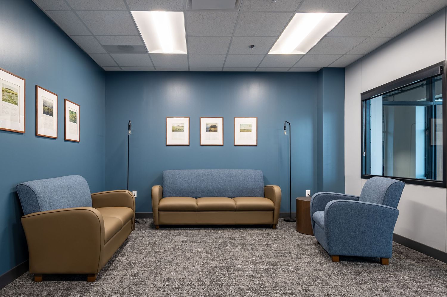 Modern office lounge area with blue walls, comfortable seating, and carpeted floors.