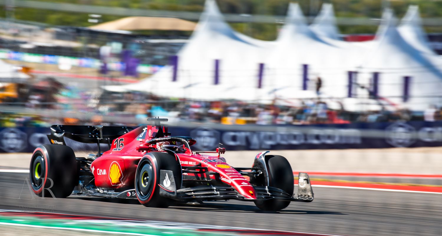 Ferrari Formula 1 car races on track with white tents visible in background.