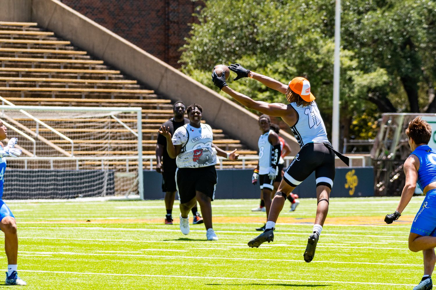 Athletes compete in a track and field event on a sunny day with stadium seating visible in background.