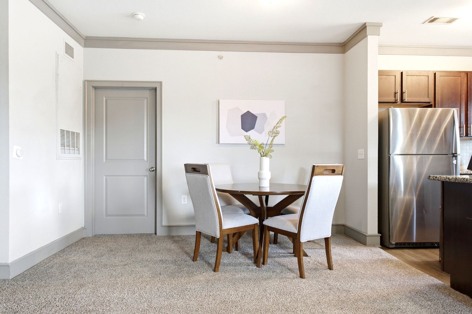 Modern dining area with glass table, white chairs, and stainless steel refrigerator in an open-concept apartment layout.
