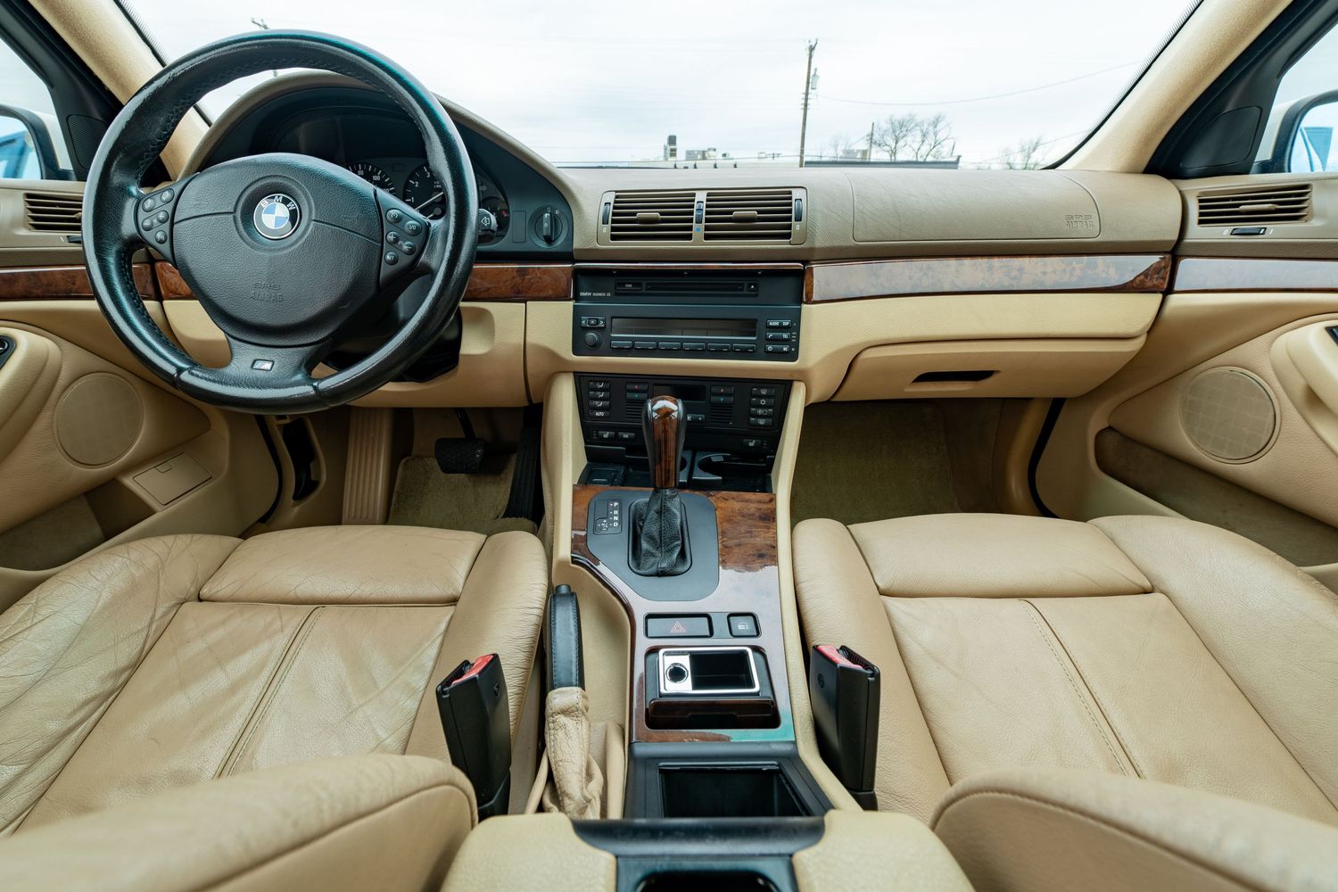 Beige leather interior of a BMW 5 Series with wood trim dashboard, automatic shifter, and dual-zone climate controls.