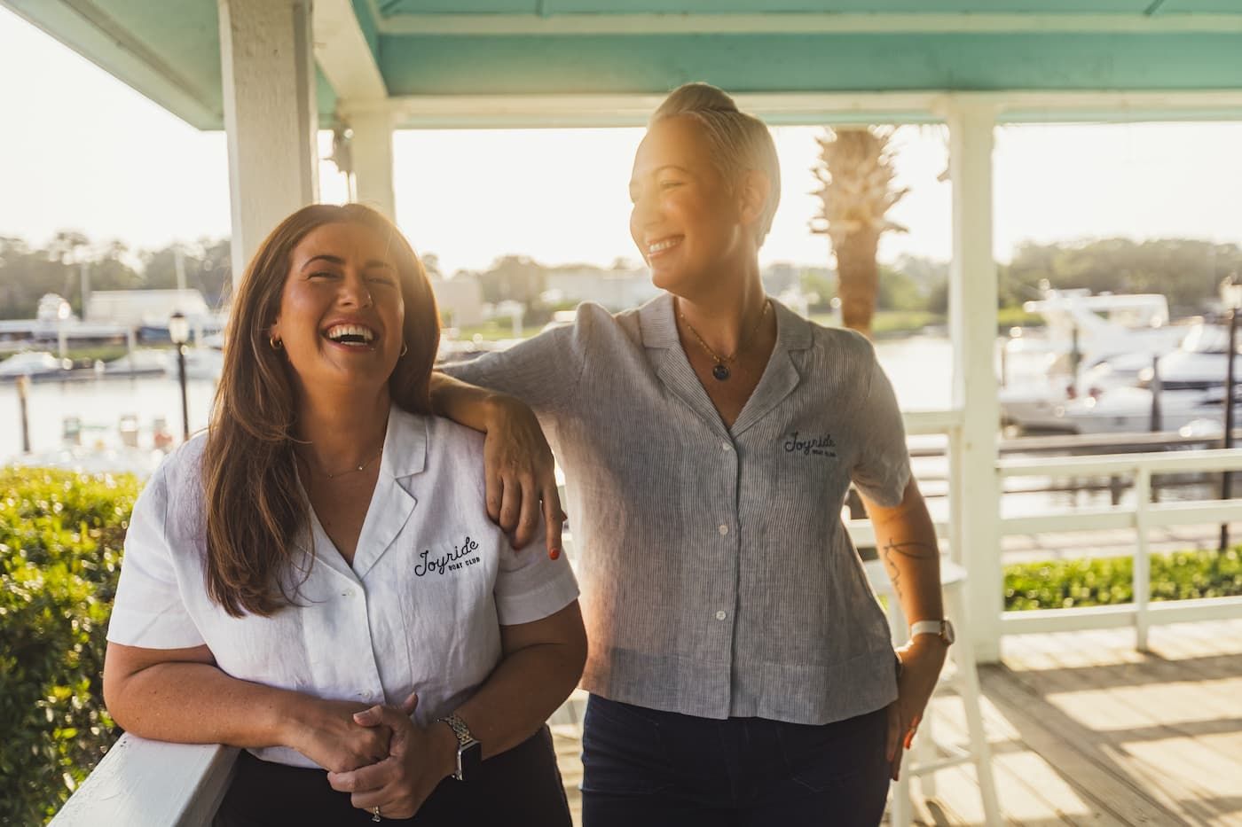 Two women in uniforms laughing together at sunny marina waterfront location.