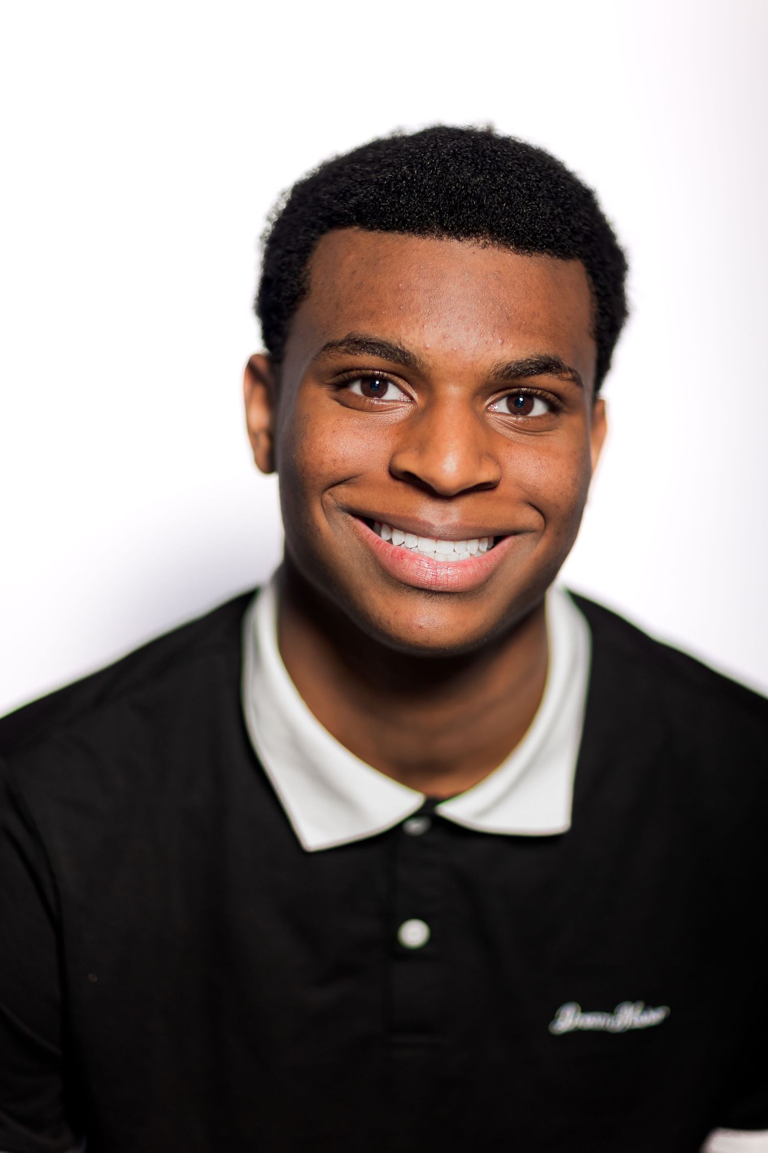 Smiling young Black man wearing a black polo shirt against a white background.