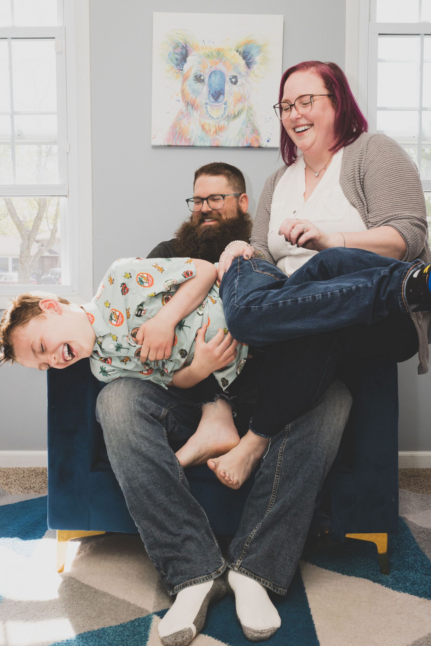 Savannah portrait photographer David Monroe —Playful family moments captured on grey couch in bright room with artwork.