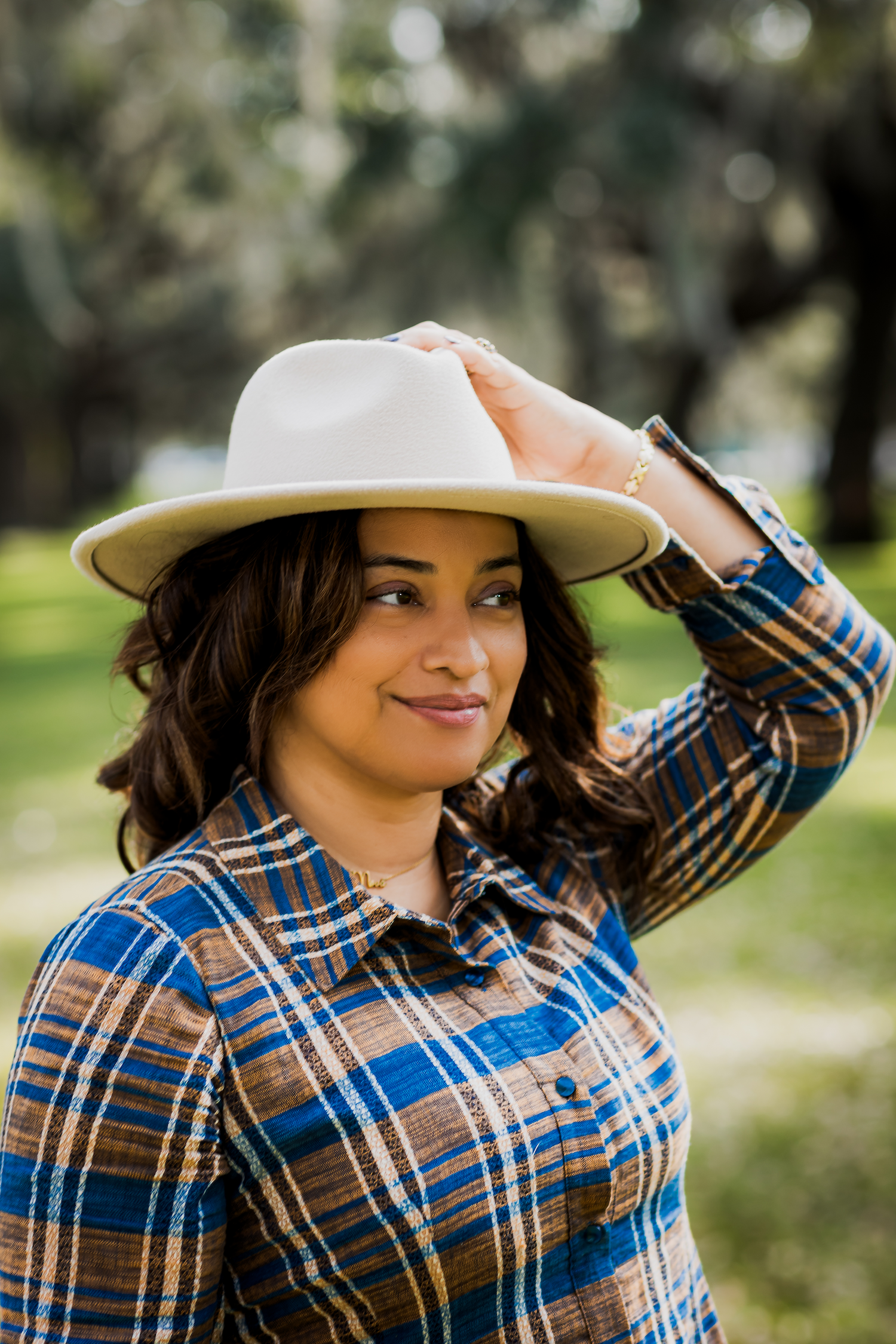 Savannah portrait photographer David Monroe — A smiling woman wearing a plaid shirt and a wide-brimmed hat stands in a park setting.