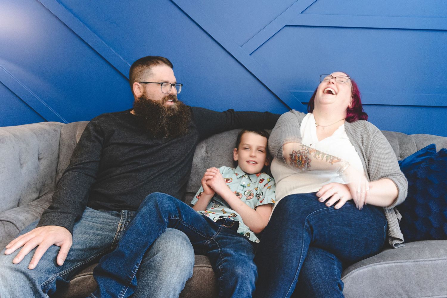 Family lounging and laughing together on blue couch during casual photo session.