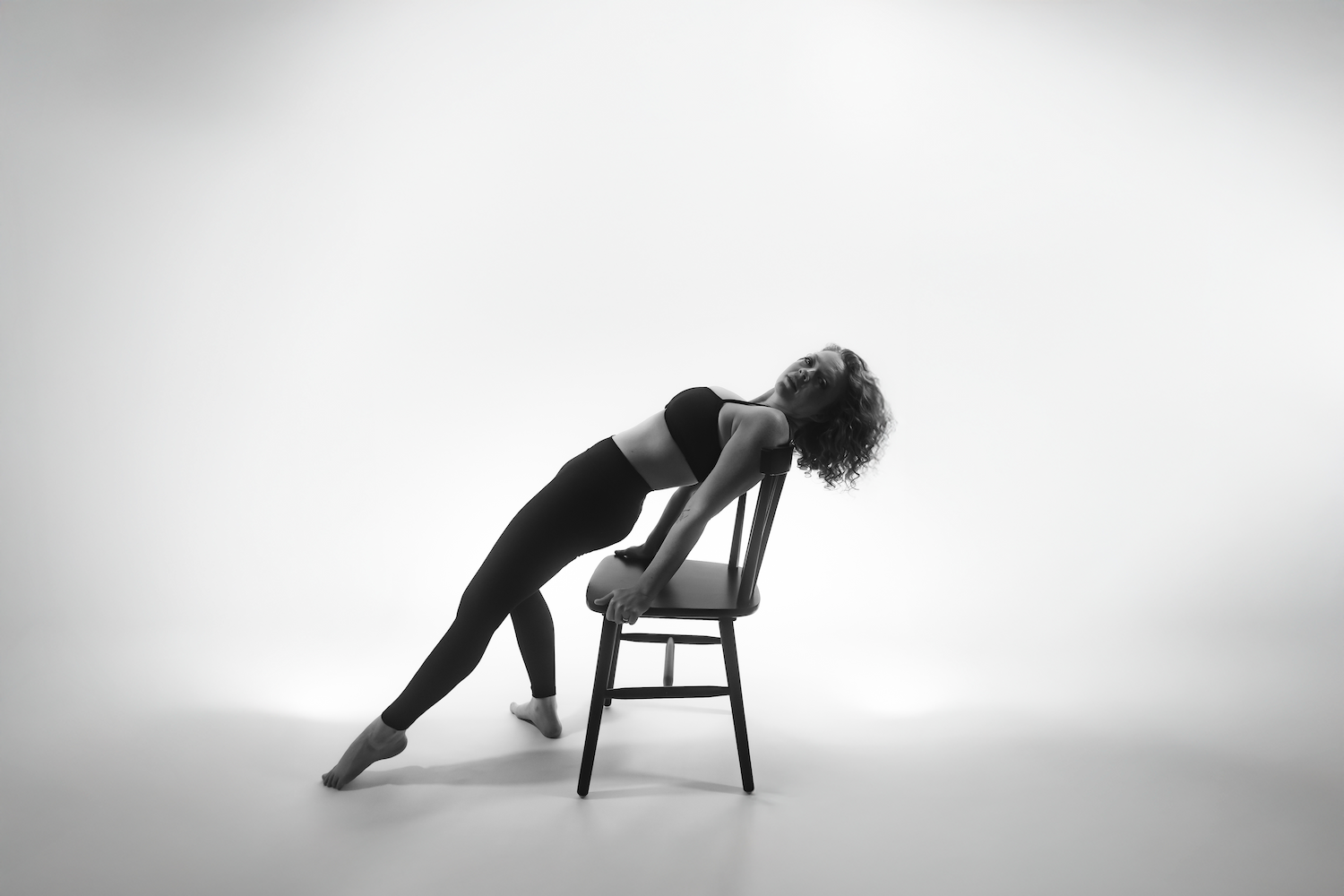 Savannah portrait photographer David Monroe — A black and white image of a person in a yoga pose on a chair against a plain background.