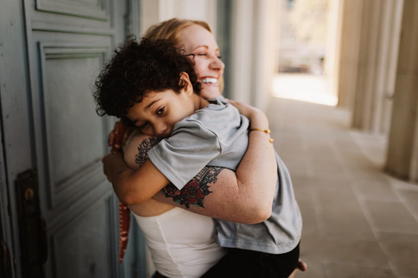 Two women sharing a warm embrace and laughing together outdoors near a blue door.
