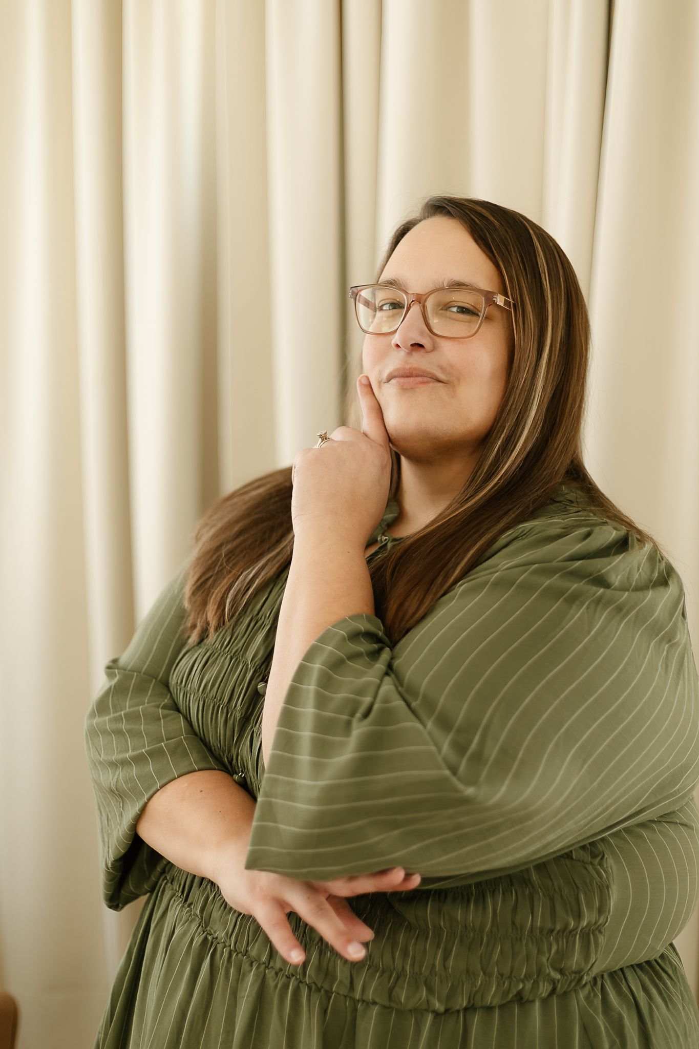 A woman in a sage green top smiles warmly while posing against a cream-colored curtain backdrop indoor studio, elkton SD