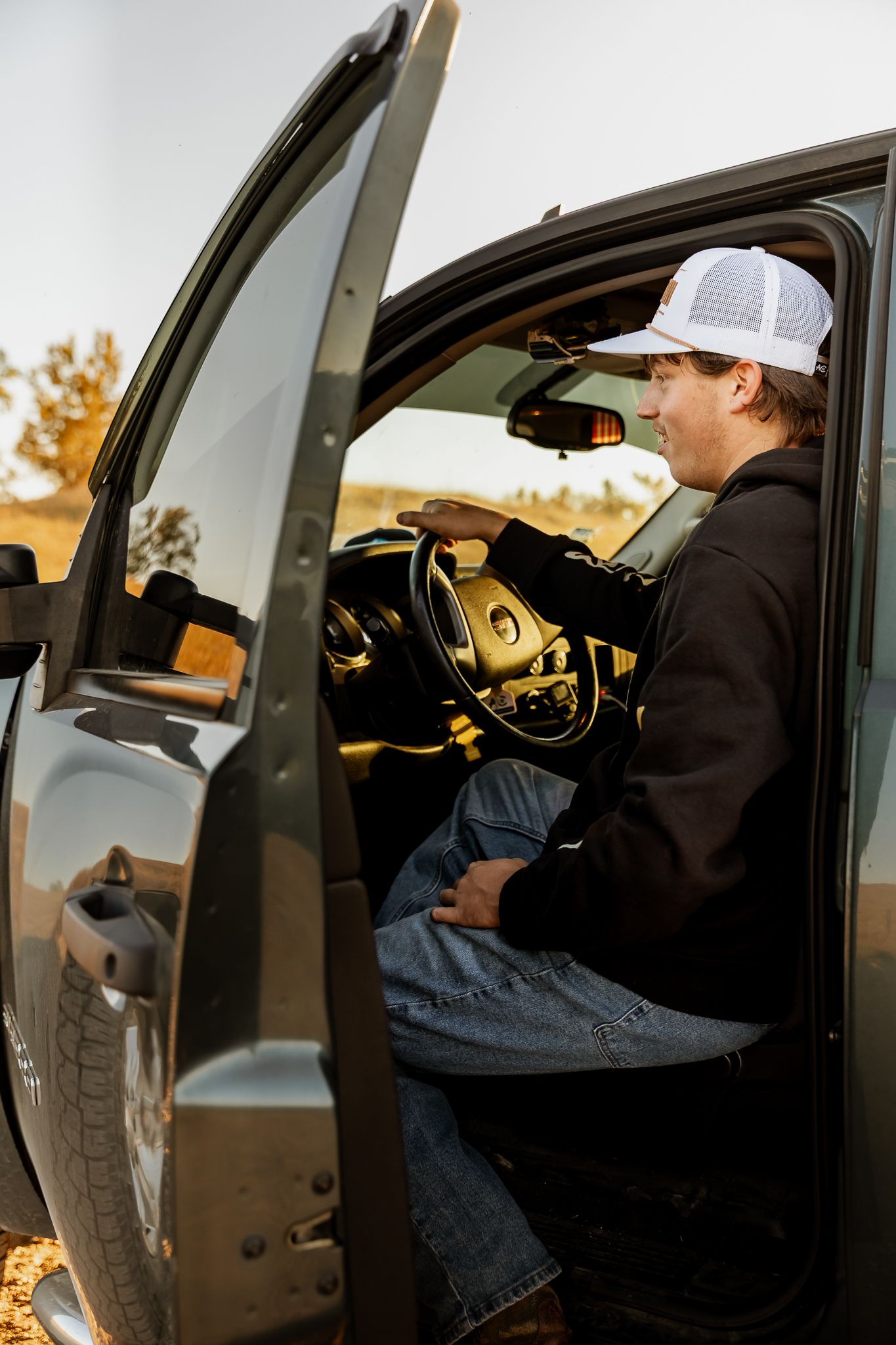 Senior wearing baseball cap shown in sequence of photos entering and sitting in driver's seat of dark vehicle at sunset, Lake Benton, MN