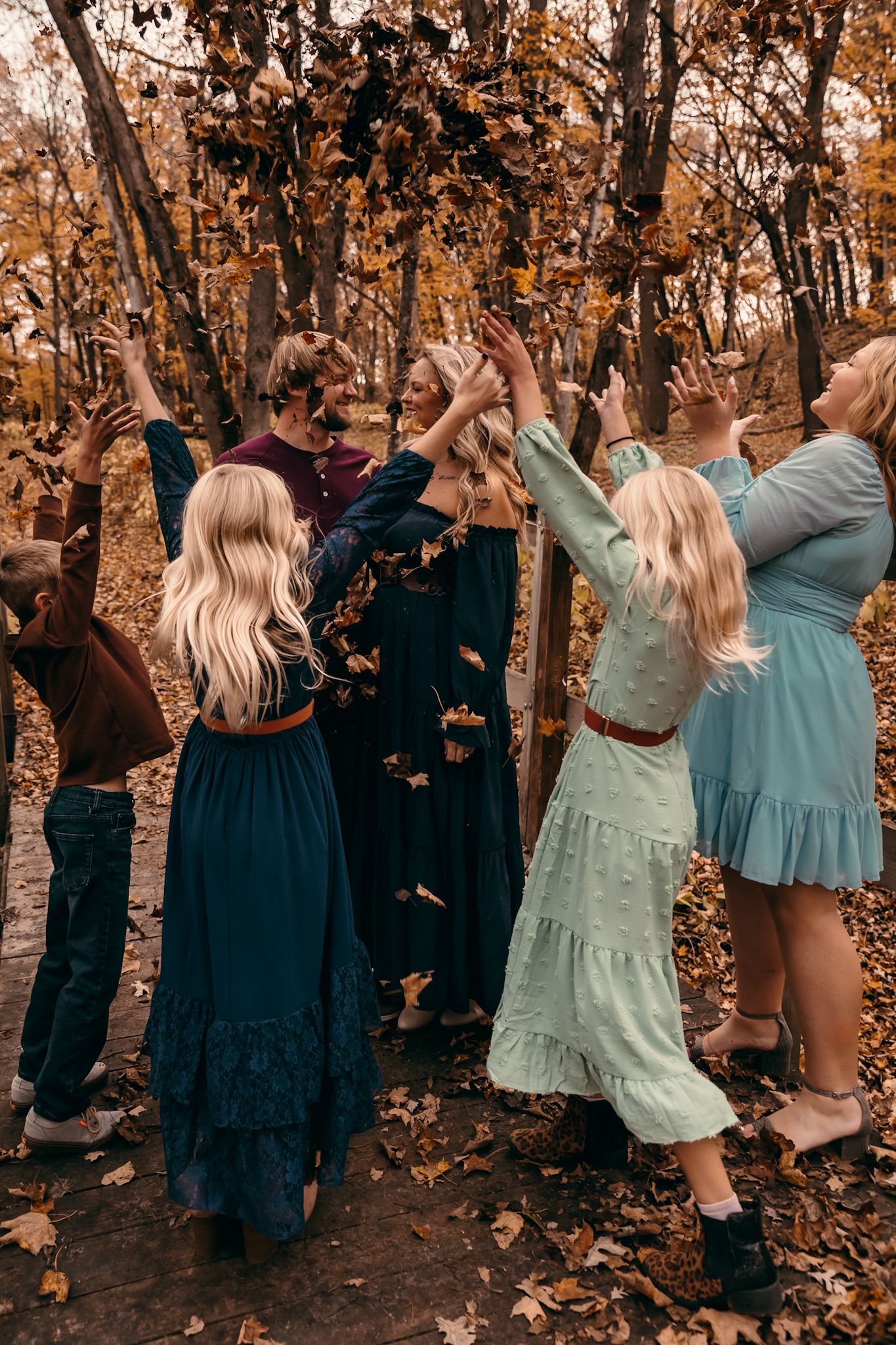 A family in formal attire throws autumn leaves in a forest during a photoshoot with warm fall colors in Lynd MN at Camden State Park