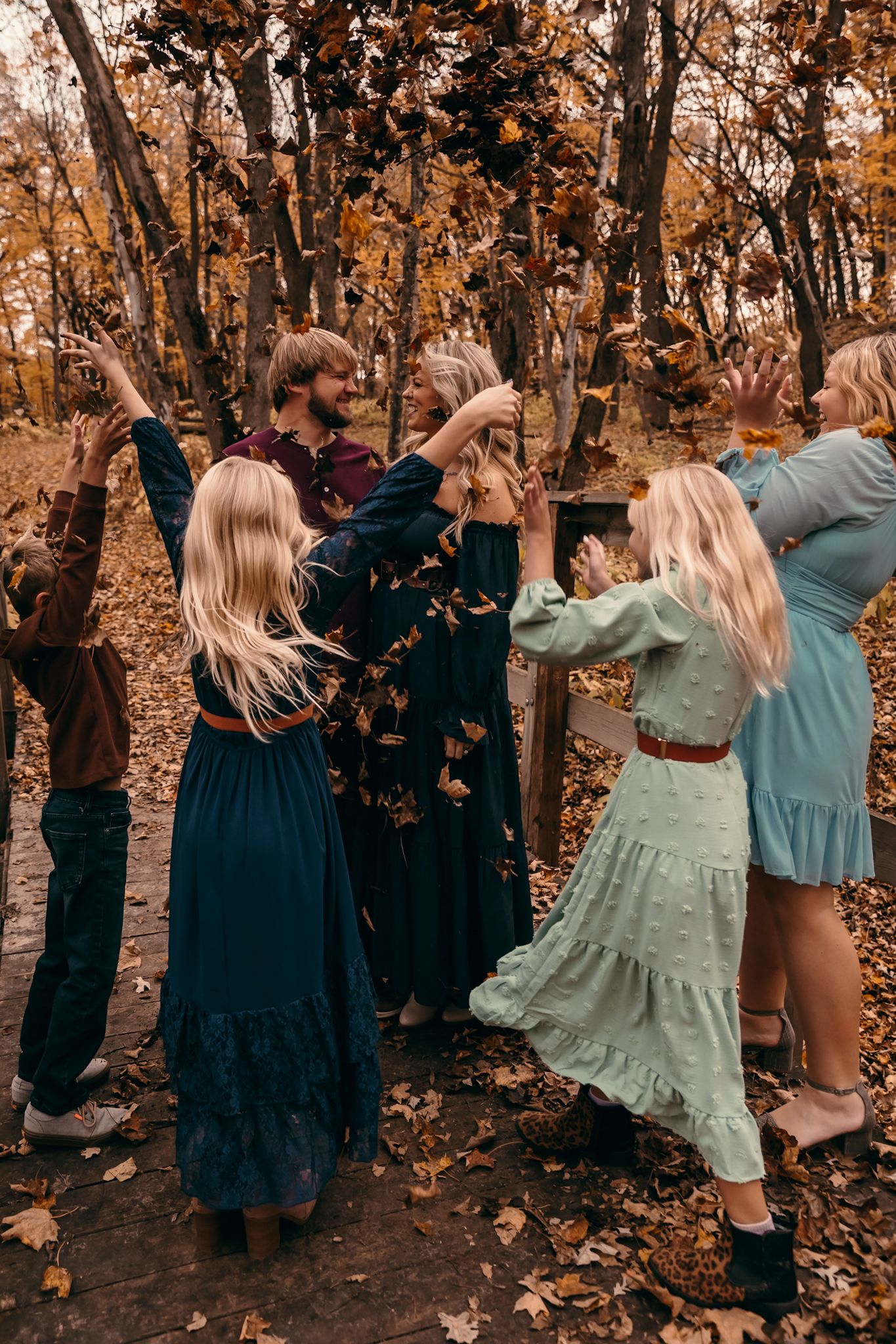 A family in formal attire throws autumn leaves in a forest during a photoshoot with warm fall colors in Lynd MN at Camden State Park