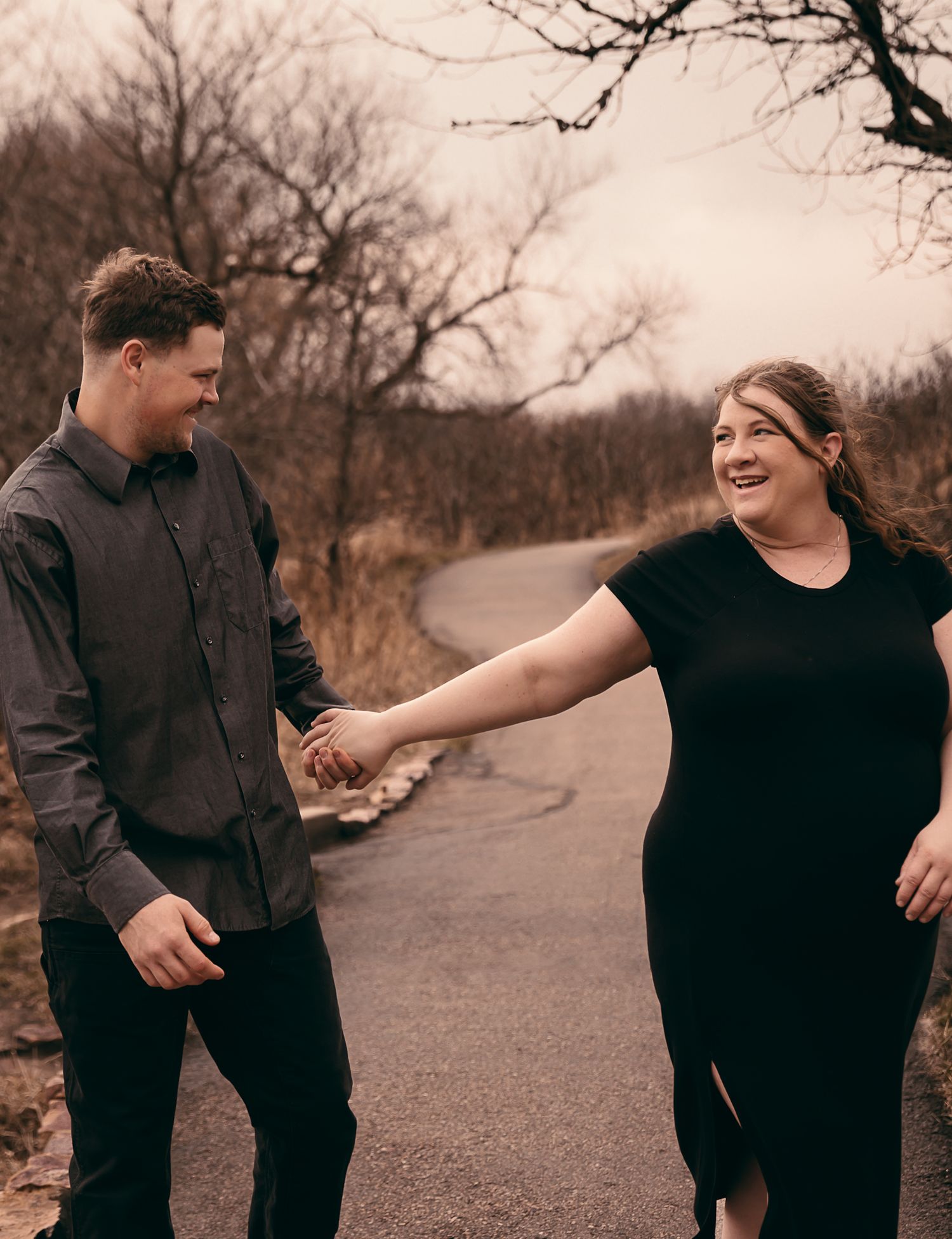 A couple holding hands while walking a path on an overcast day celebrating the pregnancy of their first child in pipestone MN