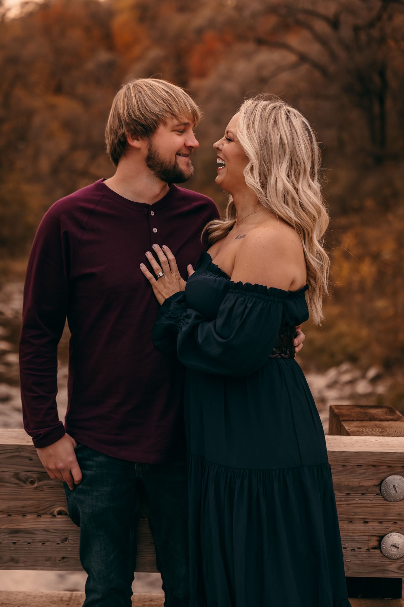 A couple in coordinating burgundy & black outfits share intimate moments during an autumn outdoor photoshoot in Lynd MN at Camden State Park
