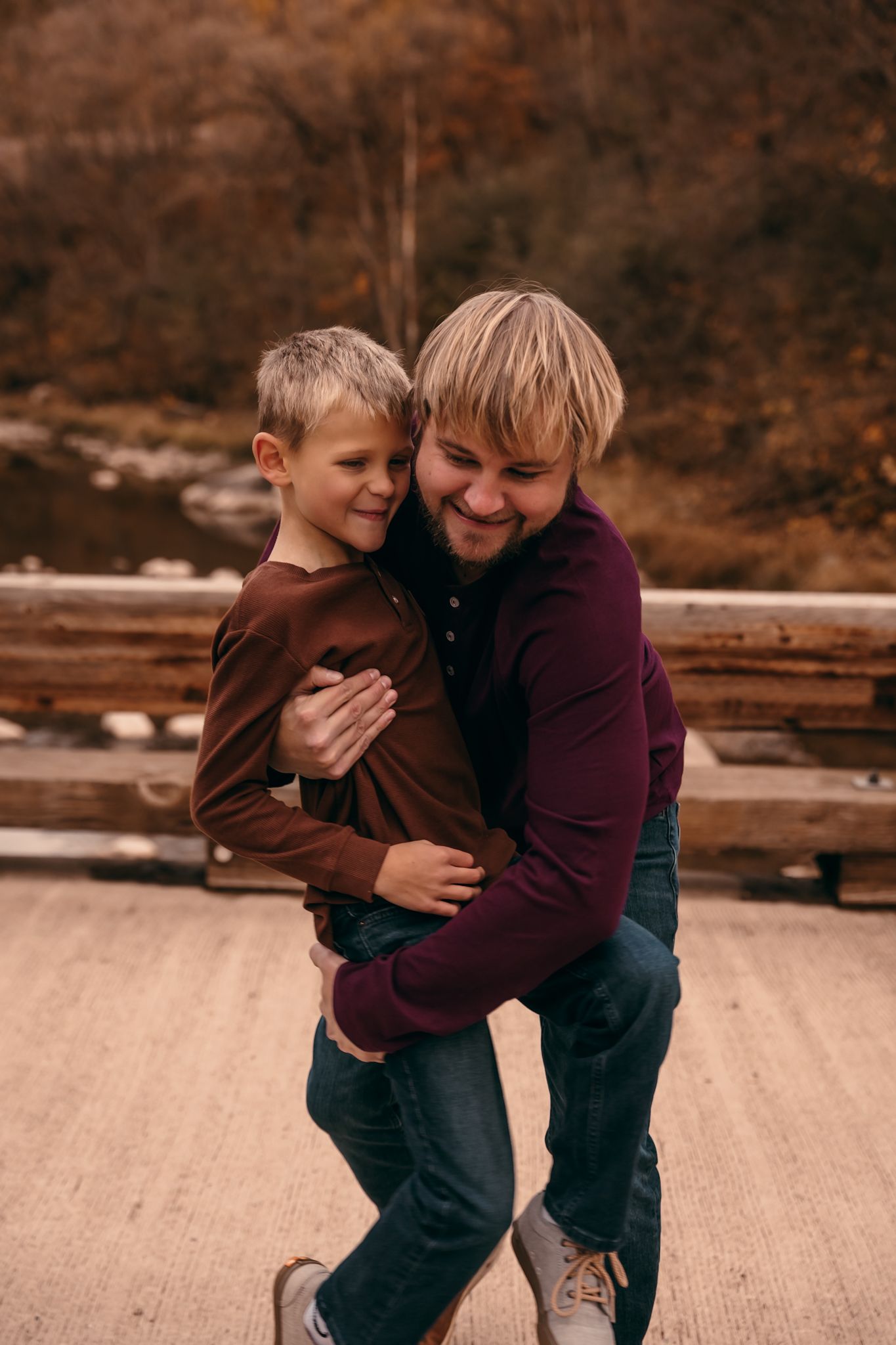 A son and father share a joyful embrace while standing on a wooden deck during autumn in Lynd MN at Camden State Park