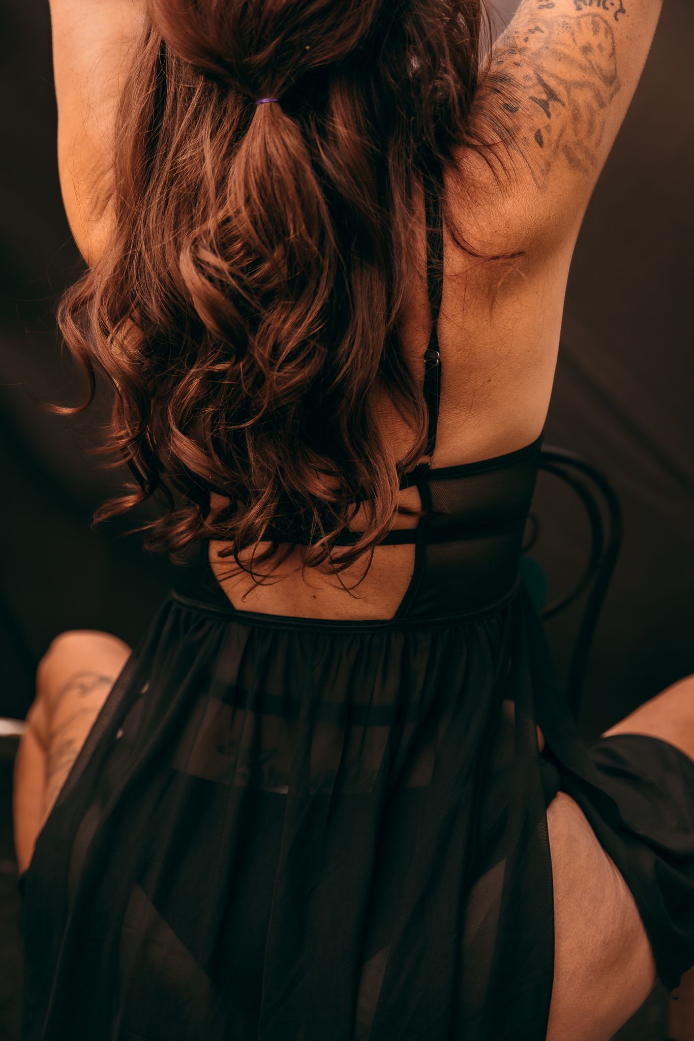 A woman with curly brown hair wearing a black dress shown from behind in a dark moody setting outdoors in Brookings, SD.