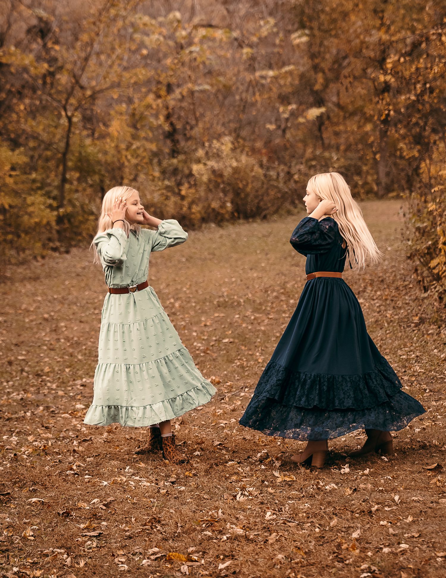 two young sisters wearing long dresses twirling together on fallen autumn leaves in a forest setting outdoor in Lynd MN