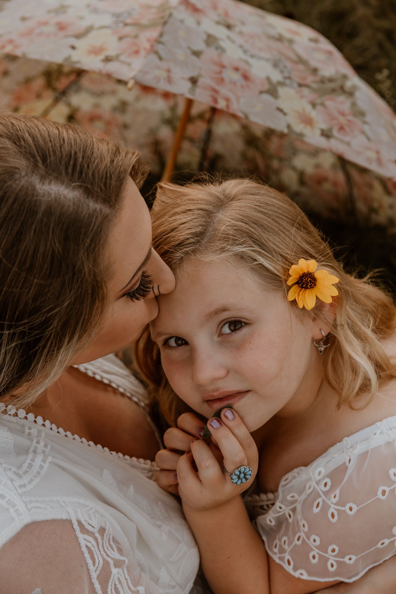 A tender moment captured between mom and daughter in white lace dresses with a yellow sunflower accent in lake benton MN, outdoor.