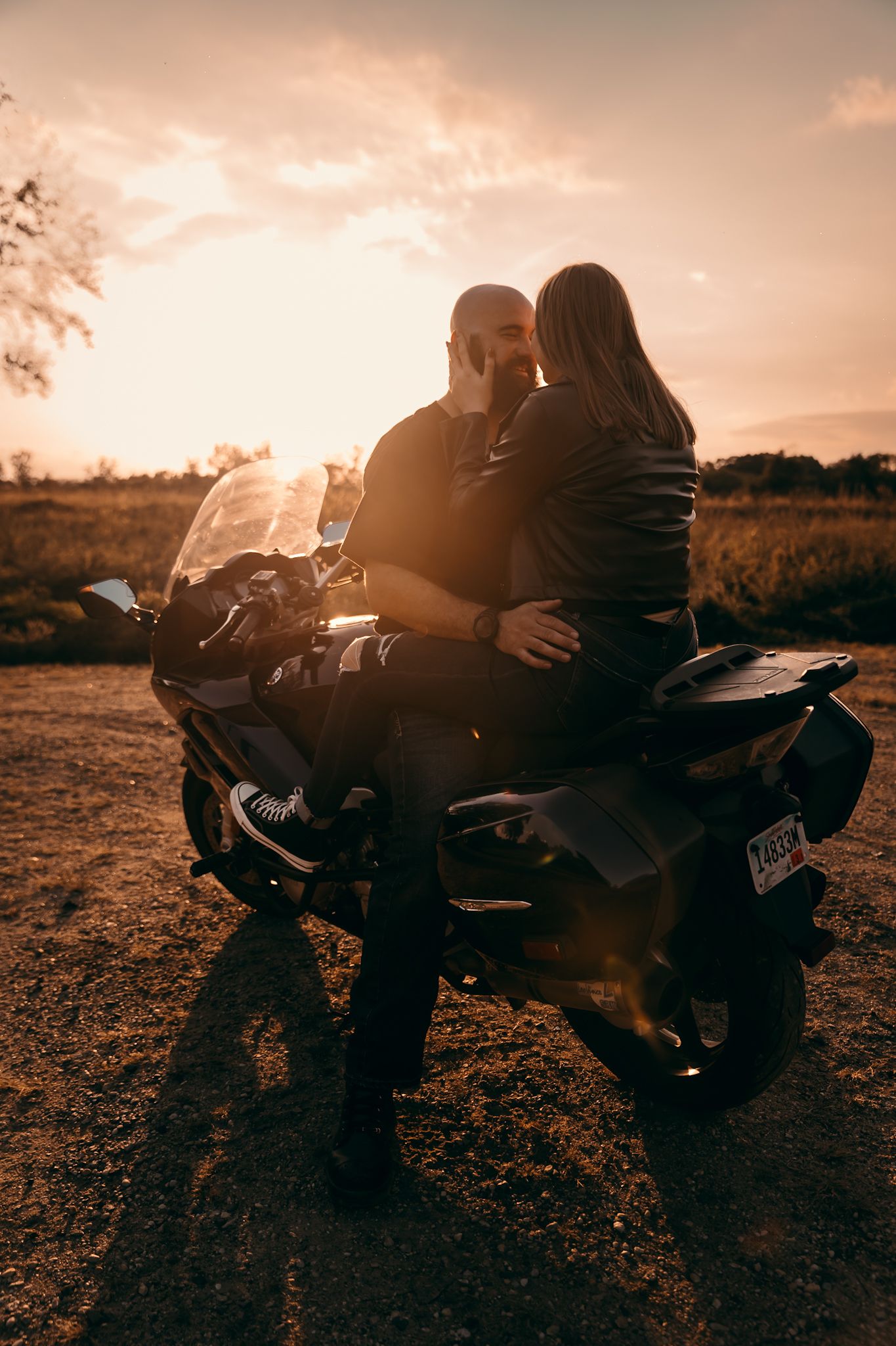 Silhouetted couple sharing intimate engagement at sunset while sitting on motorcycle in Lynd, MN; camden state park