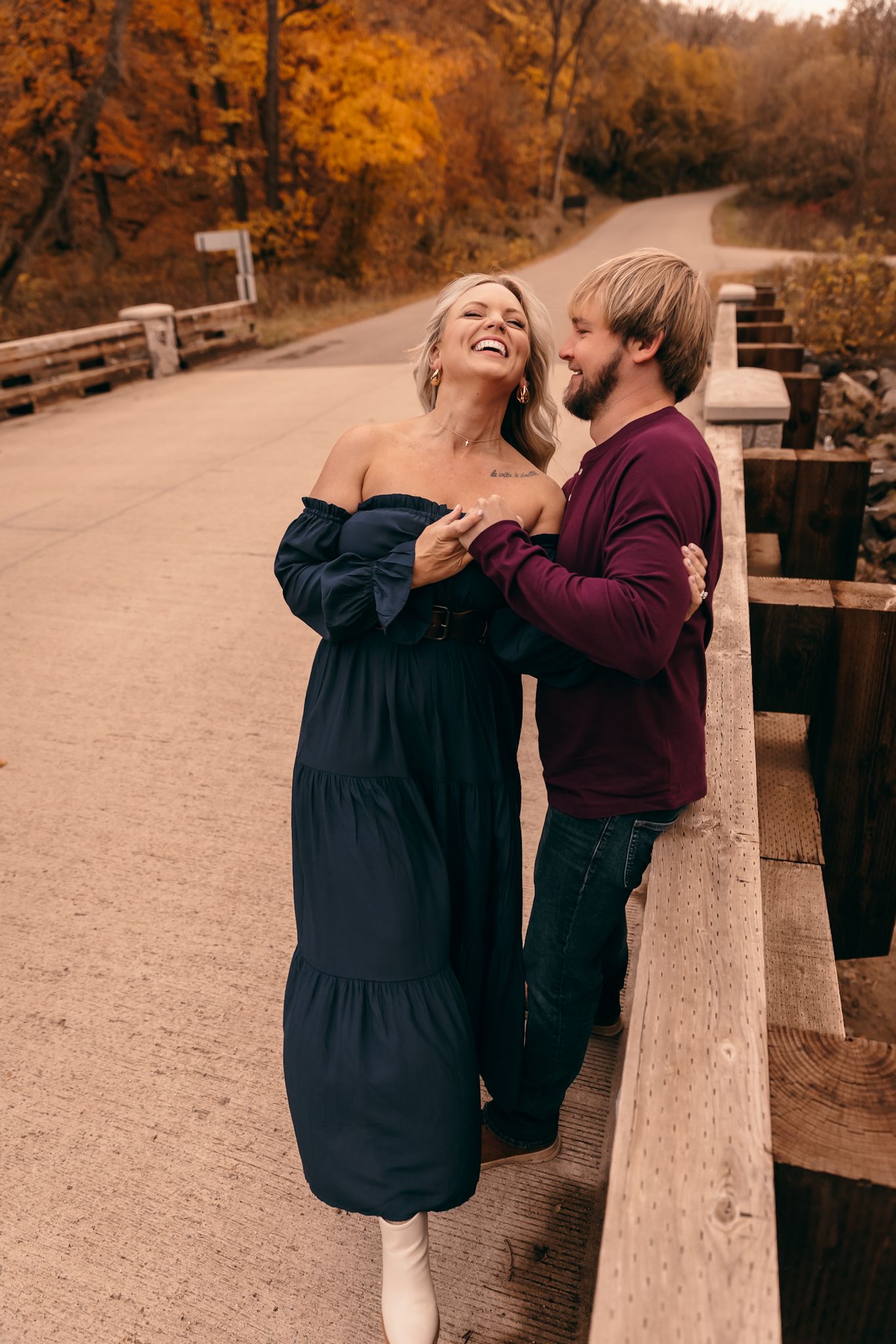 A couple shares joyful laughter together on a wooden bridge during a golden autumn afternoon in Lynd MN at Camden State Park