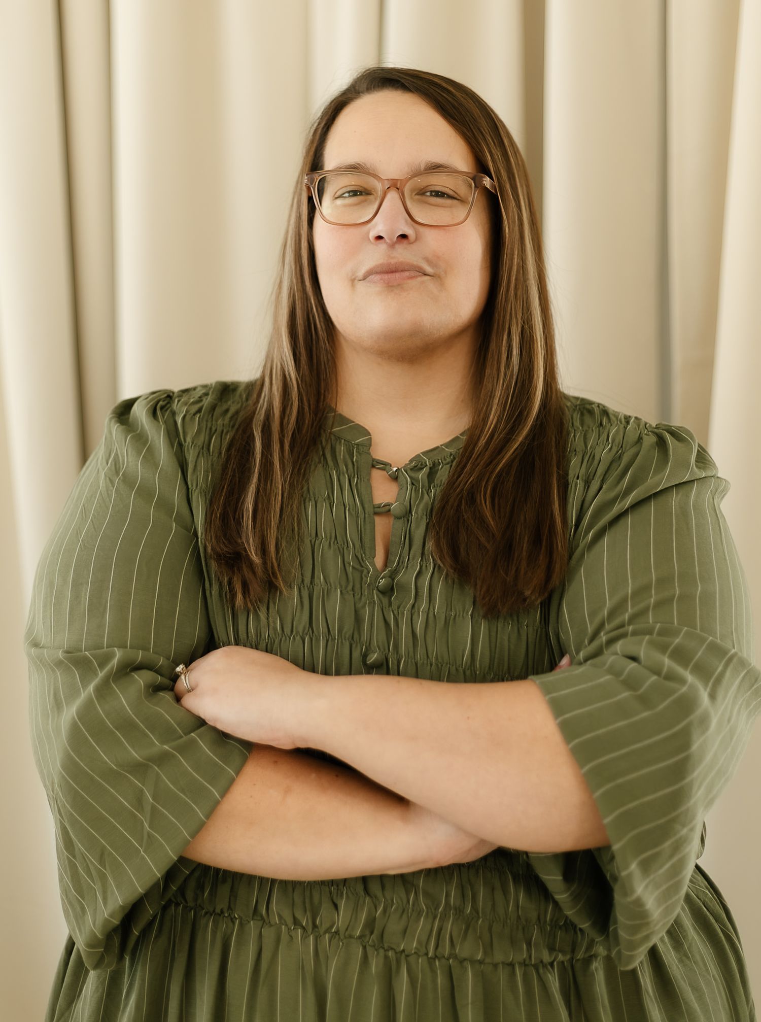 A woman in a sage green top smiles warmly while posing against a cream-colored curtain backdrop indoor studio, elkton SD
