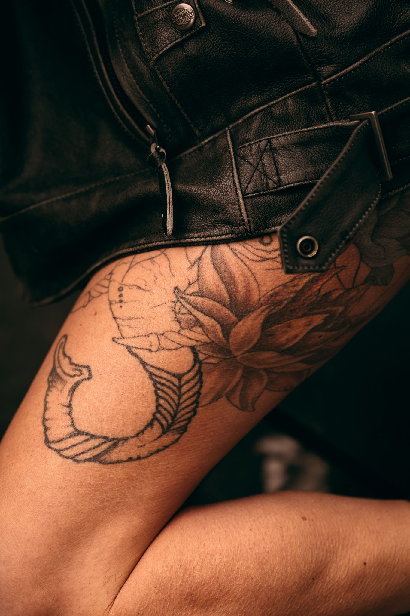Close-up view of a black leather jacket sleeve revealing floral tattoo artwork on skin underneath, outdoors in Brookings, SD