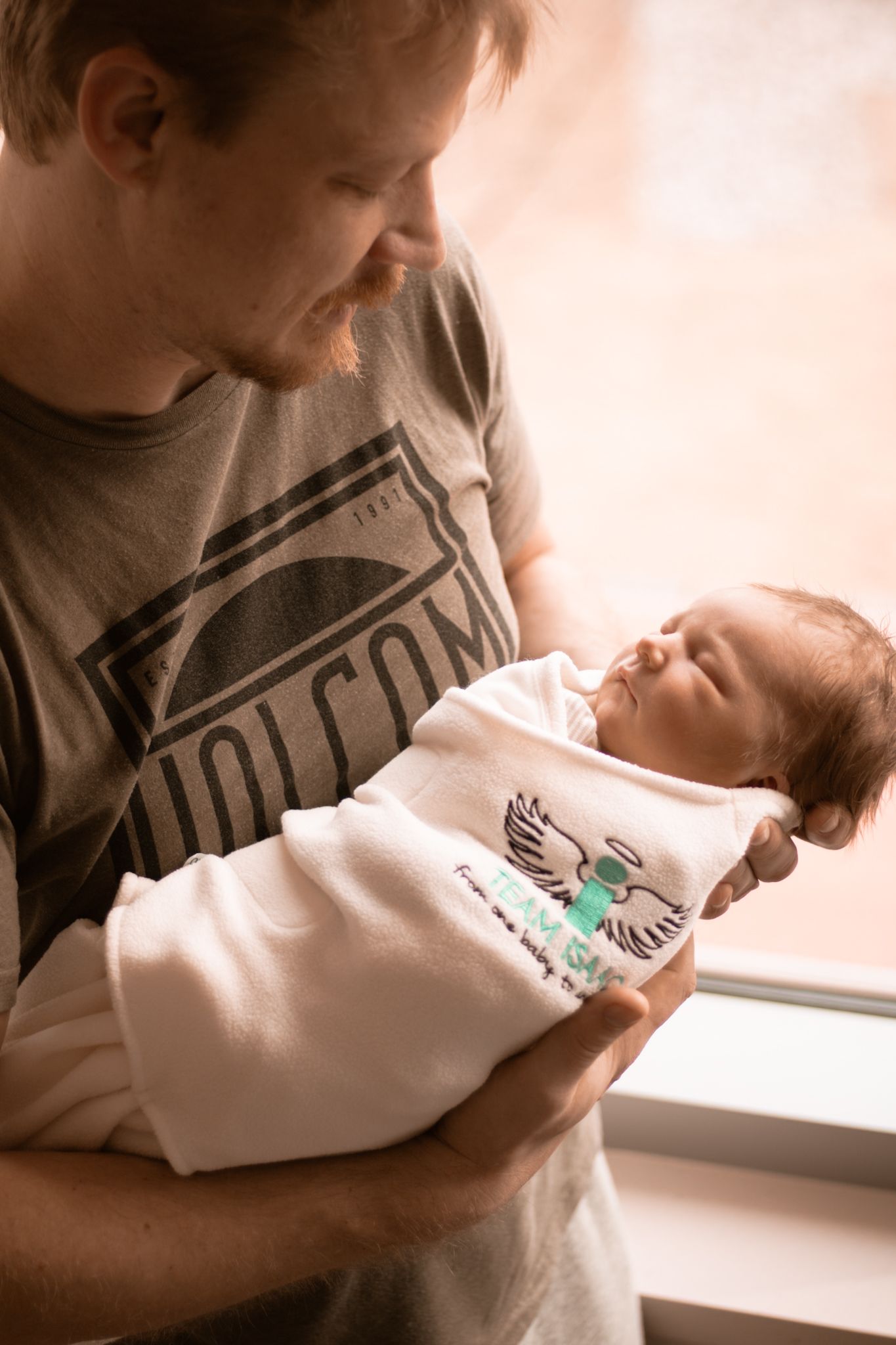 A tender moment captured in earthy tones as a first time father gazes lovingly at his sleeping newborn baby.