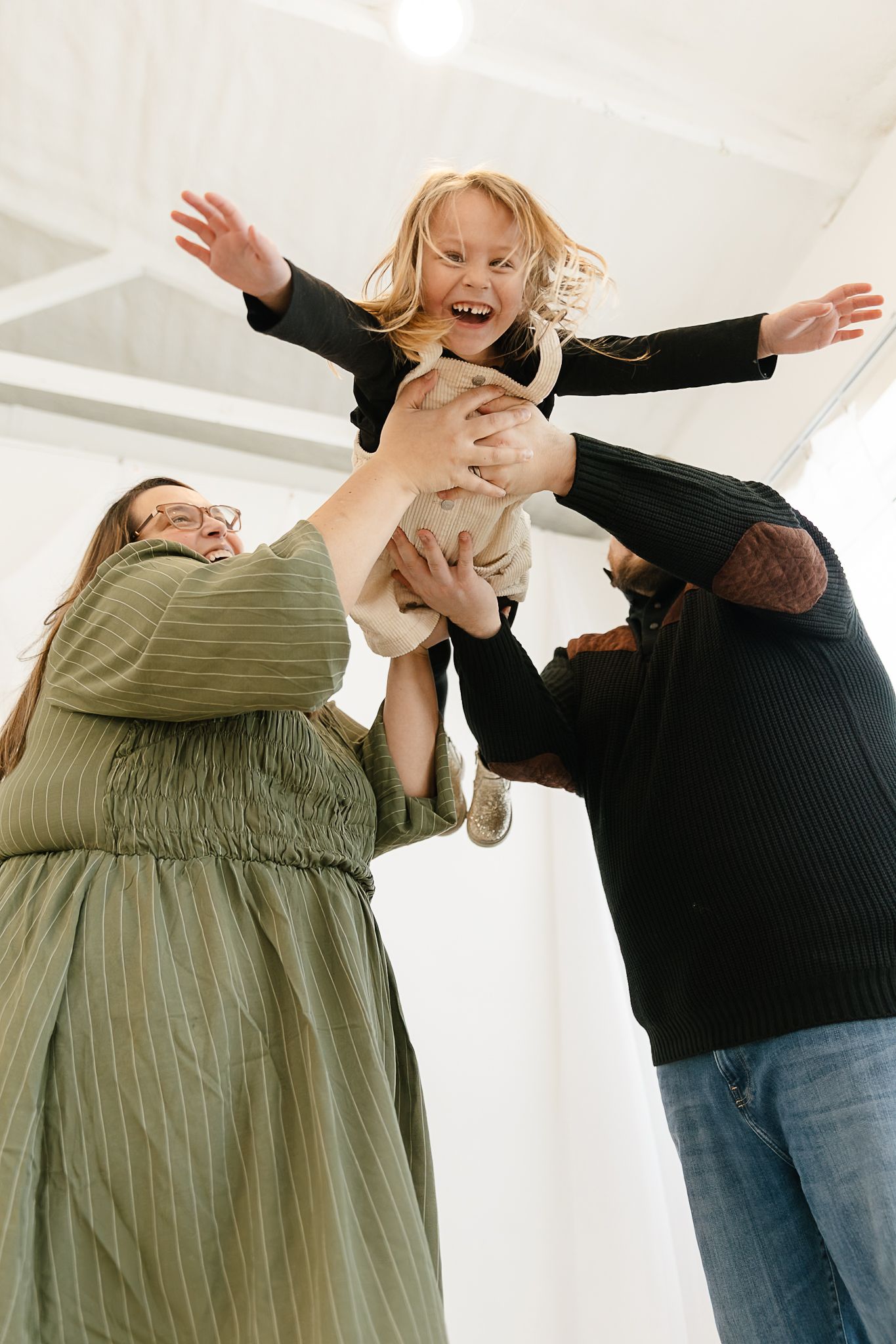 Family sharing joyful moments and laughter while flying their daughter through the air in a warmly lit studio in Elkton SD