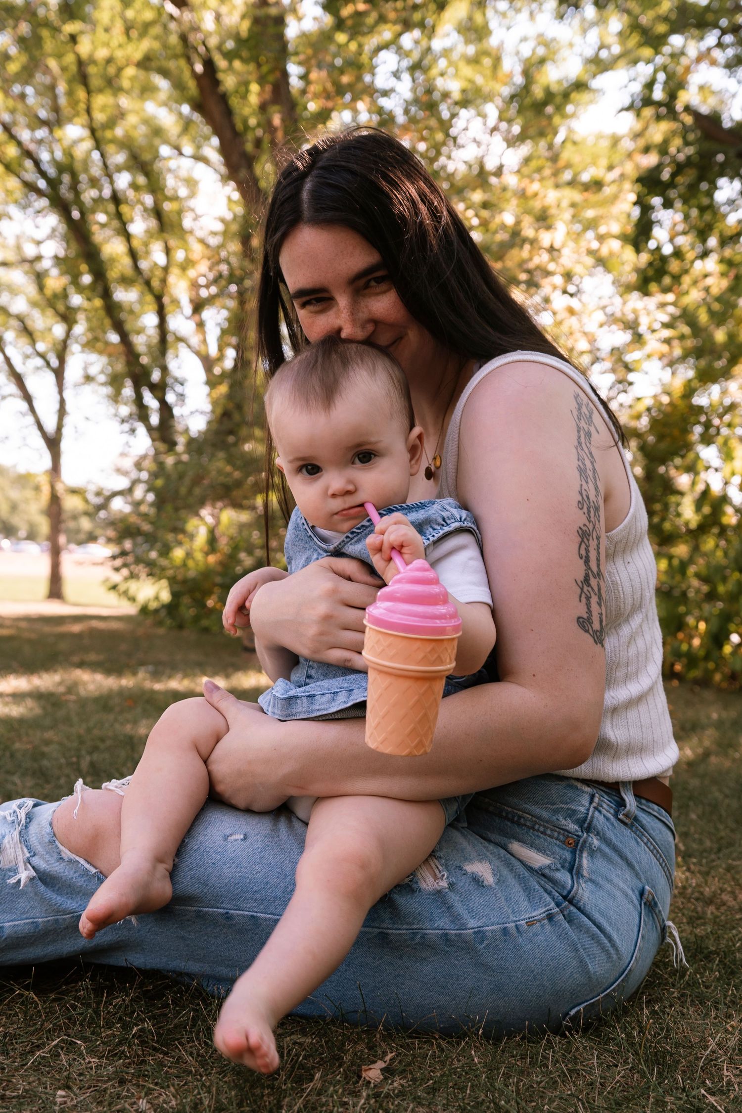 A parent and child sit in a park on a sunny day while holding a pink toy ice cream cone. Regina Saskatchewan Family portrait photographer.