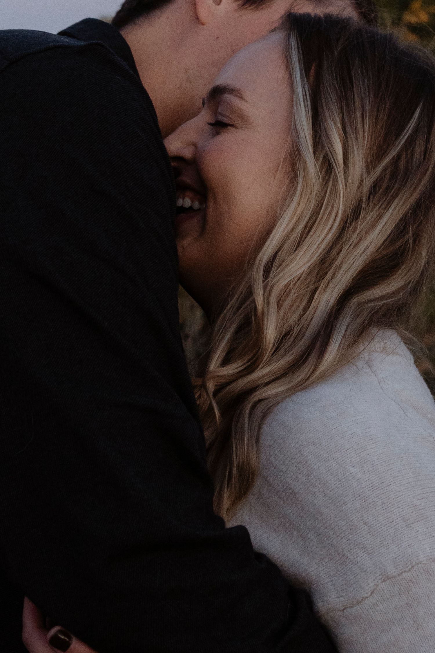 A joyful couple sharing a romantic kiss, the woman smiling with blonde wavy hair in a white sweater.
