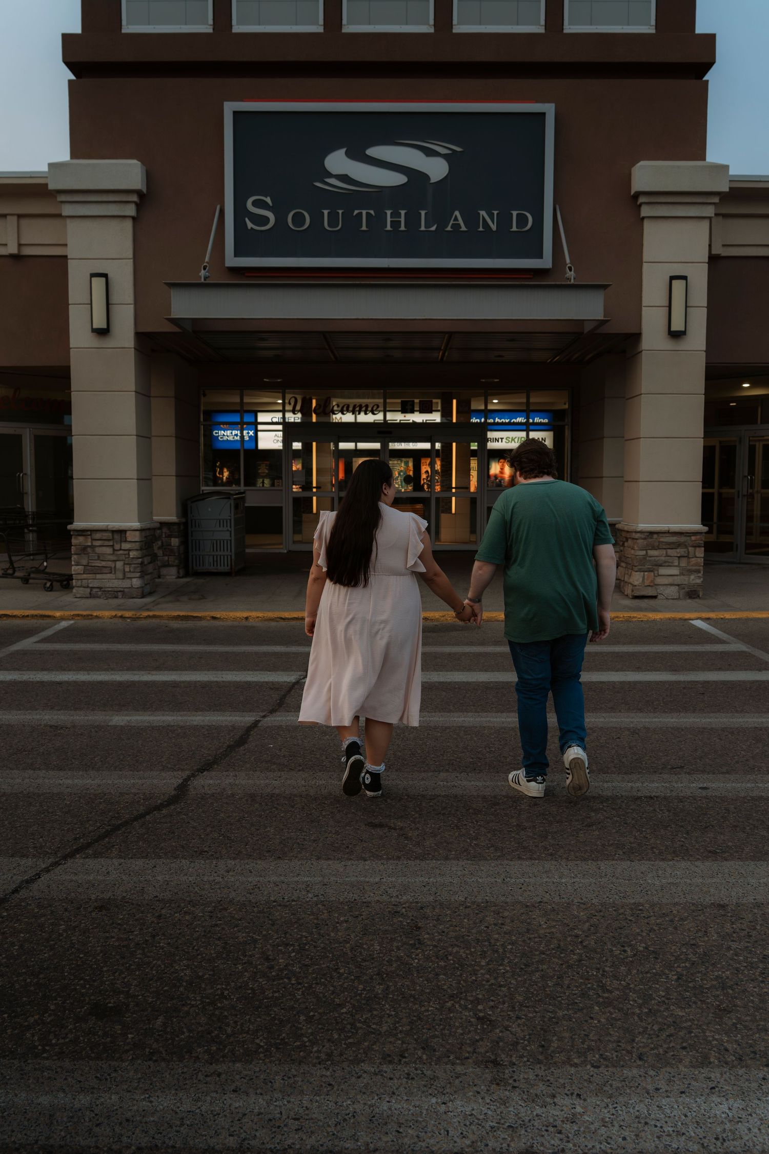 Couple holding hands walking toward Southland Mall entrance at dusk, woman in white dress and man in green shirt.