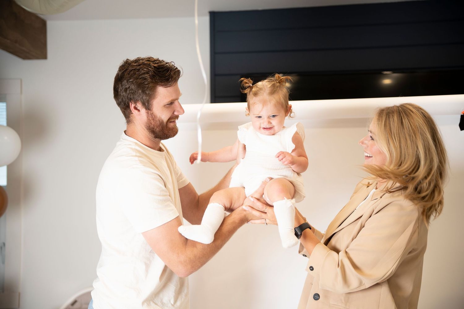 A happy couple playing with their smiling baby girl in a bright modern room.