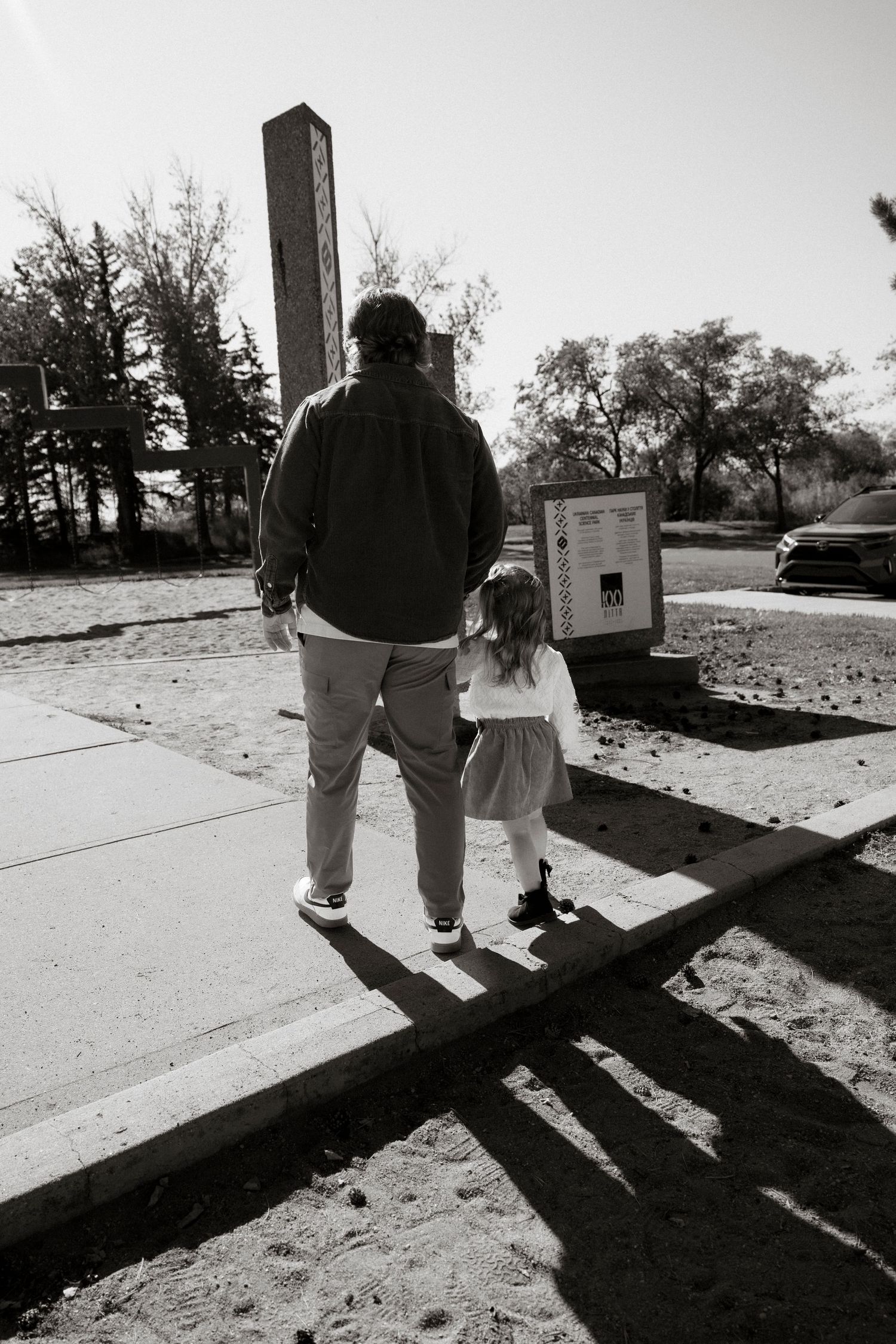 Black and white photo of an adult and young child walking hand in hand toward a monument in a park.