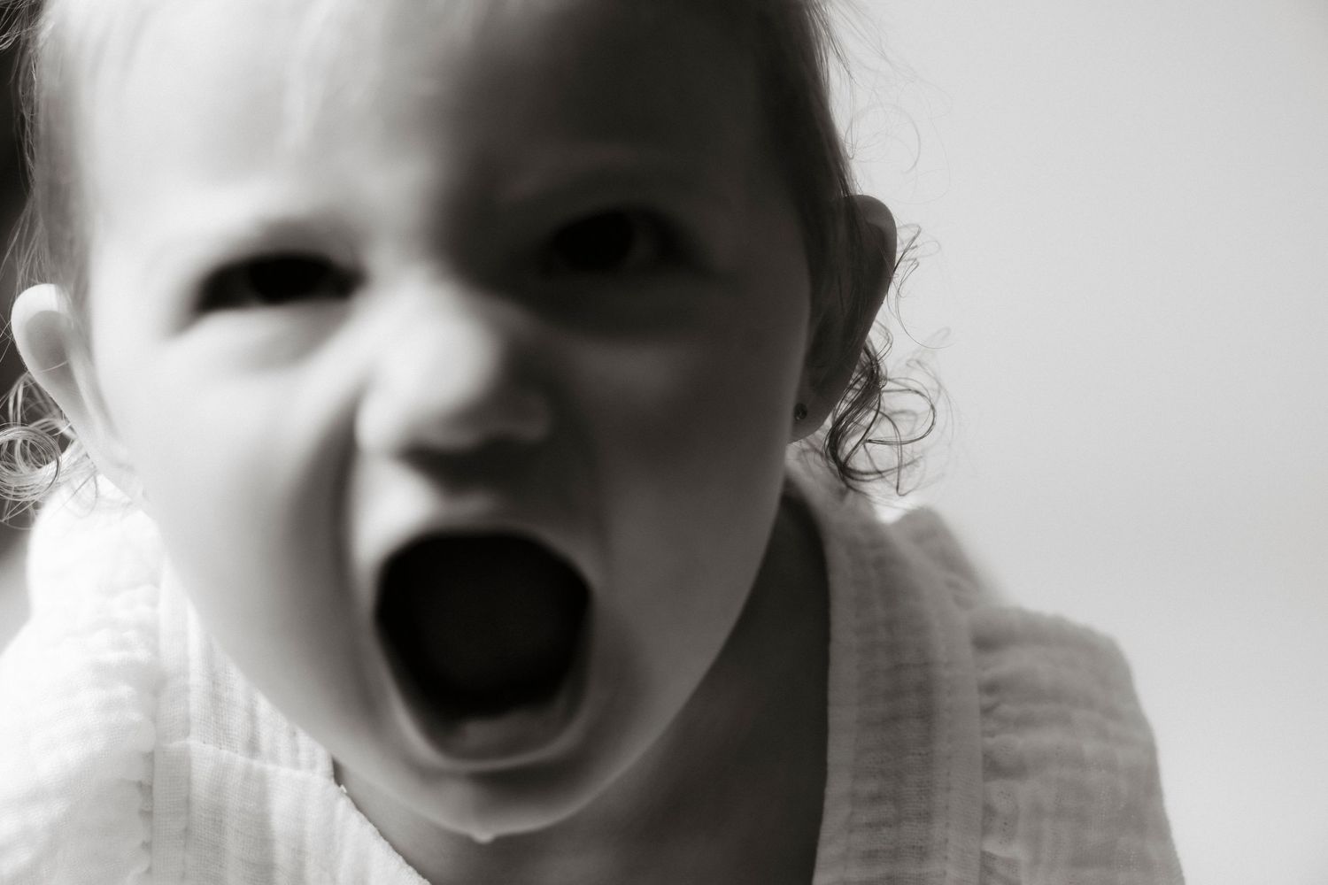 Black and white photo of a young toddler with mouth wide open, appearing to yell or scream expressively.