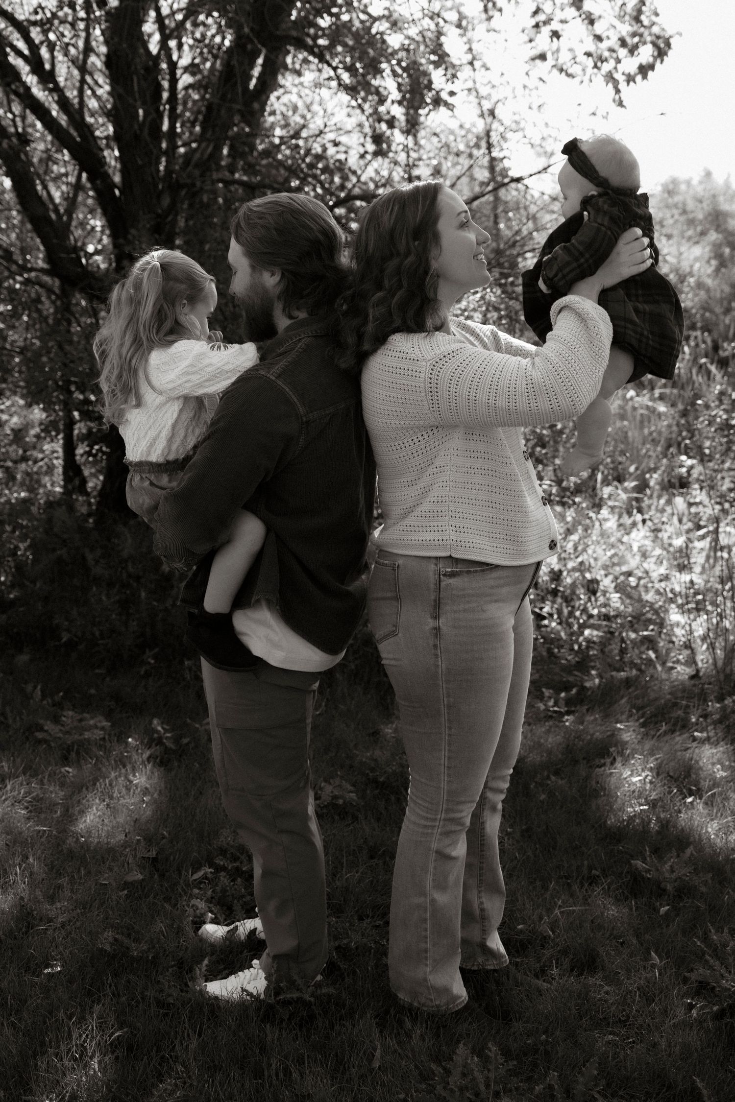 Black and white photo of a couple holding two young children outdoors among trees.
