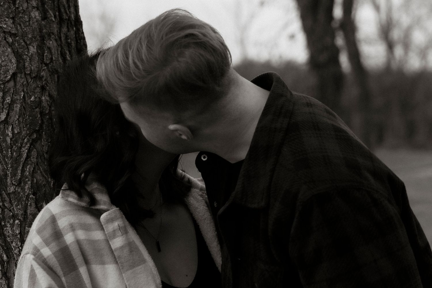Black and white photo of a couple sharing an intimate moment near a tree in an outdoor setting.