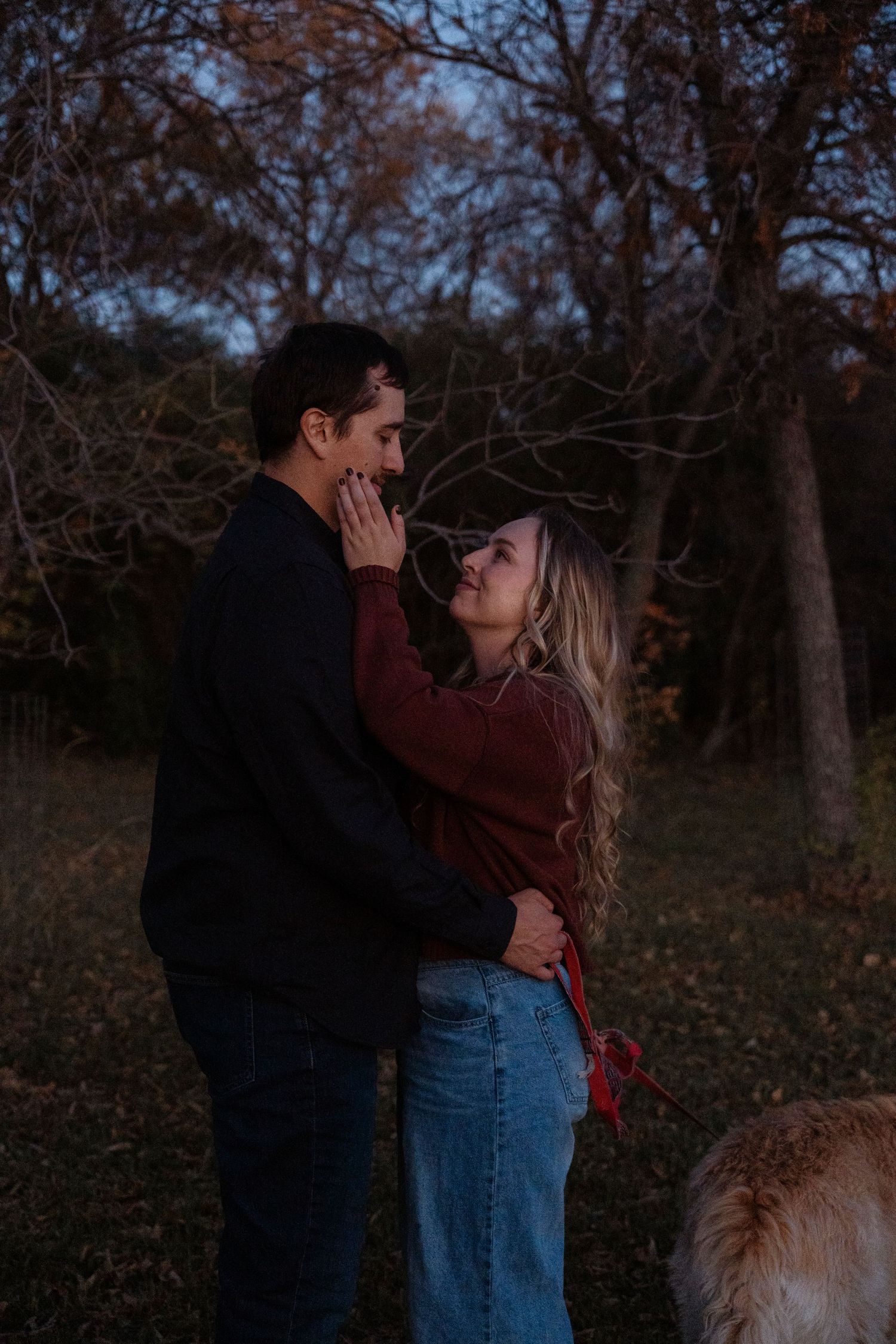 Couple sharing a romantic moment outdoors at dusk in autumn, with a golden dog nearby.