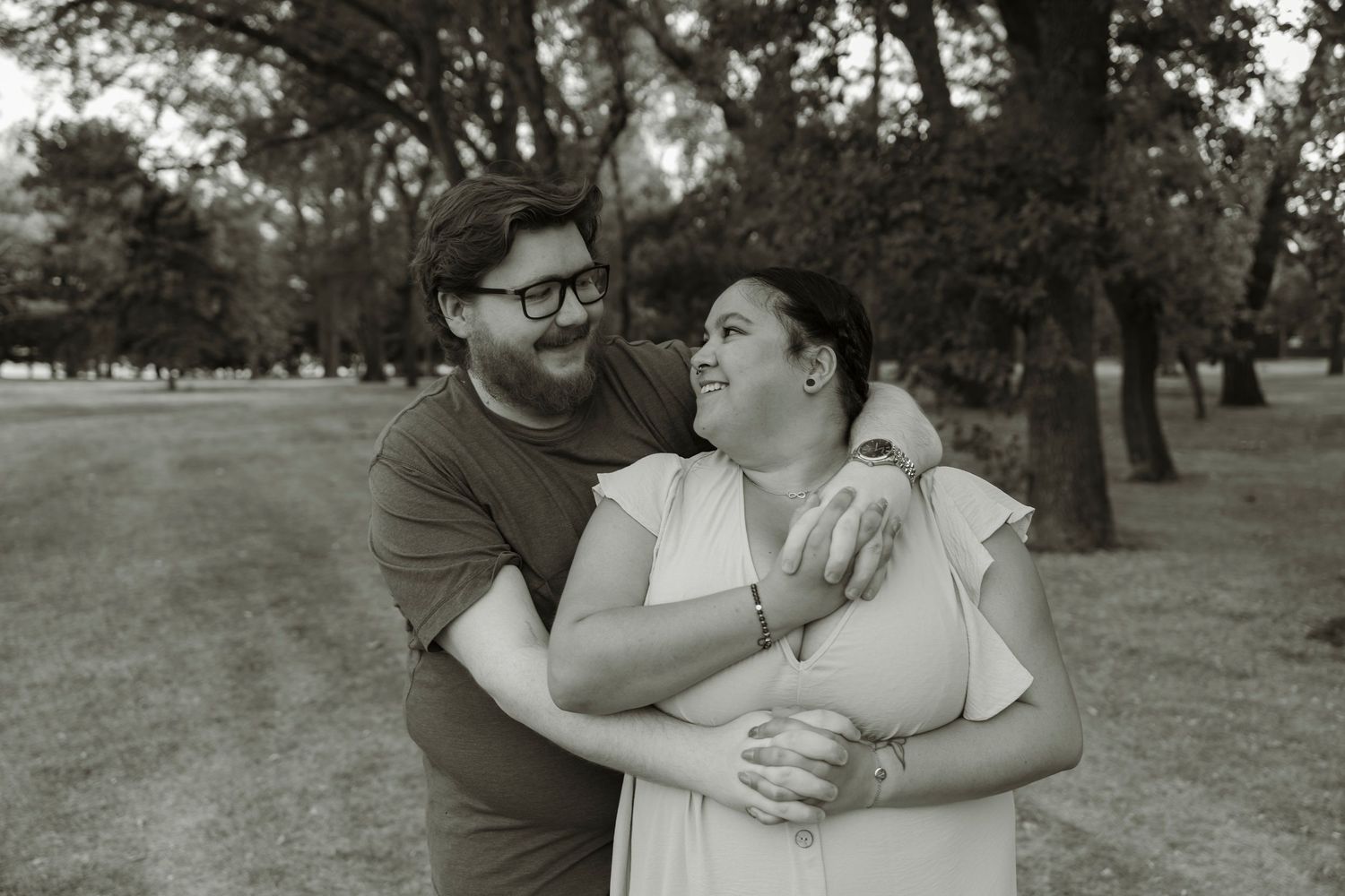 Couple embracing and smiling in a park, black and white engagement photo outdoors.