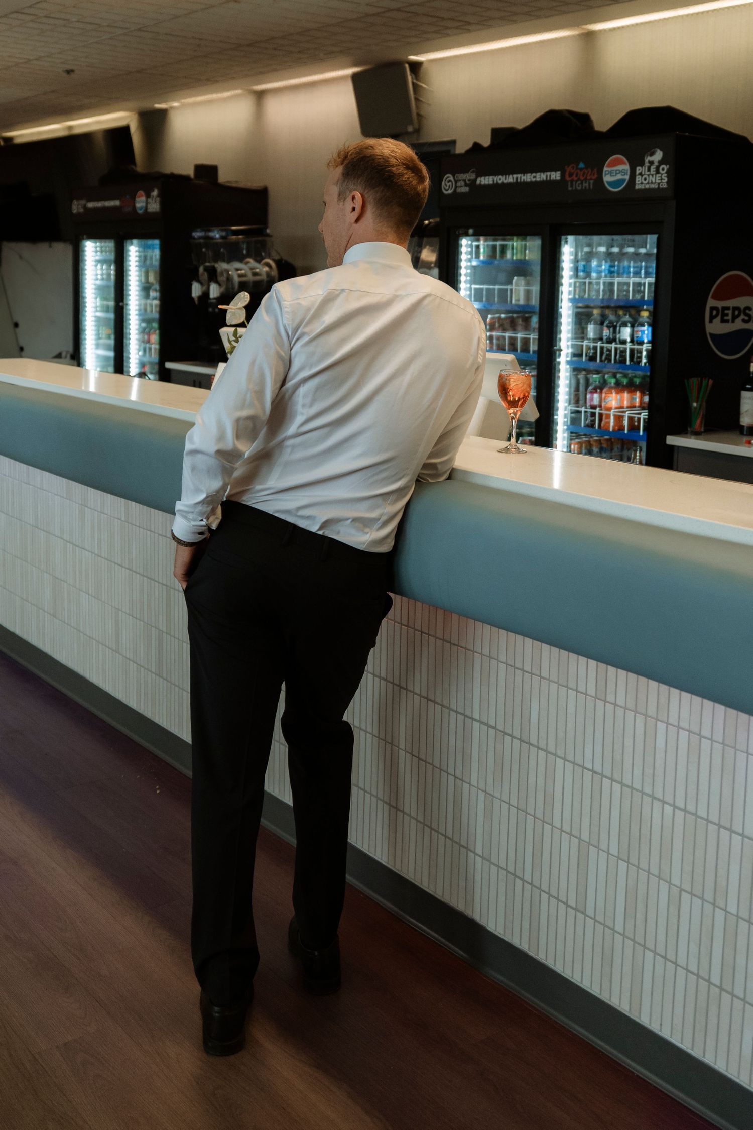 Man in white shirt standing at a Pepsi bar counter holding a drink, viewed from behind.