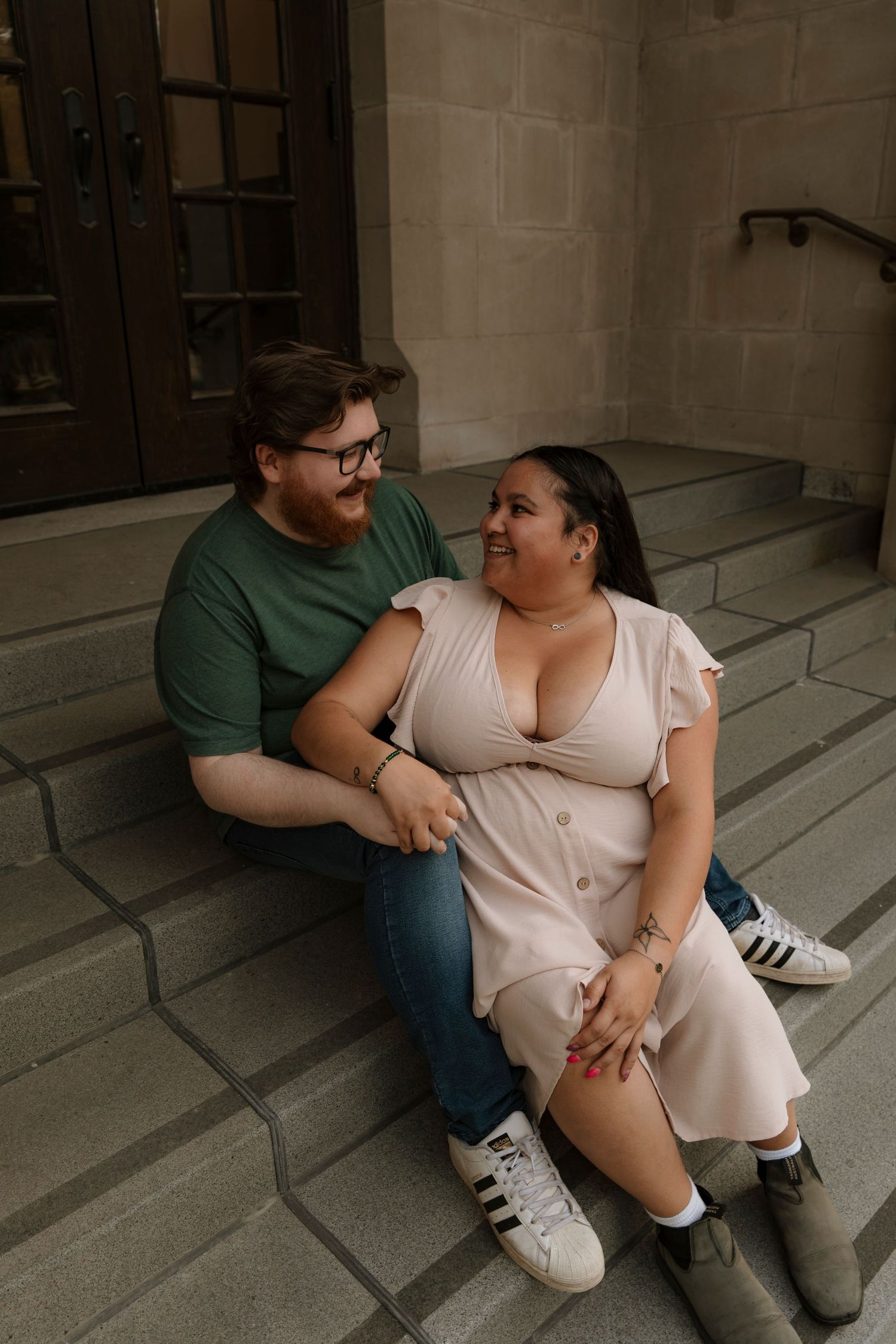 A couple sits on stone steps, smiling at each other, man in green shirt and woman in pink dress.