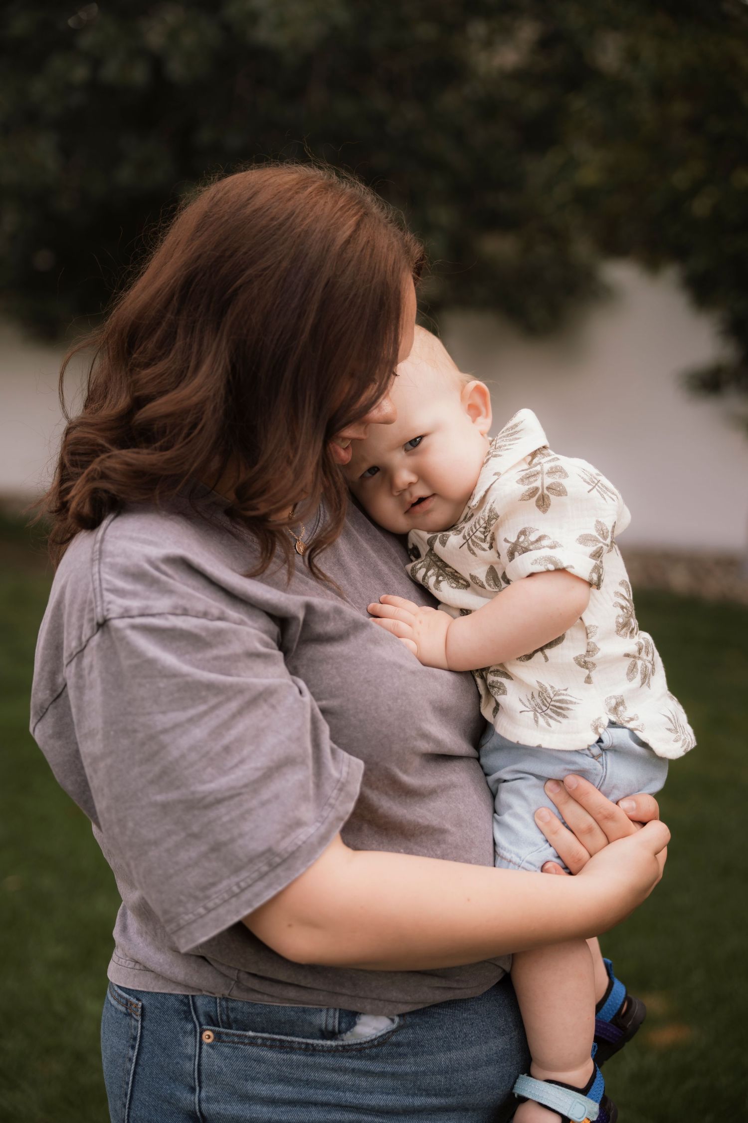 Tender embrace between adult in gray shirt and baby in patterned outfit outdoors. Regina Saskatchewan Family Portrait Photographer.