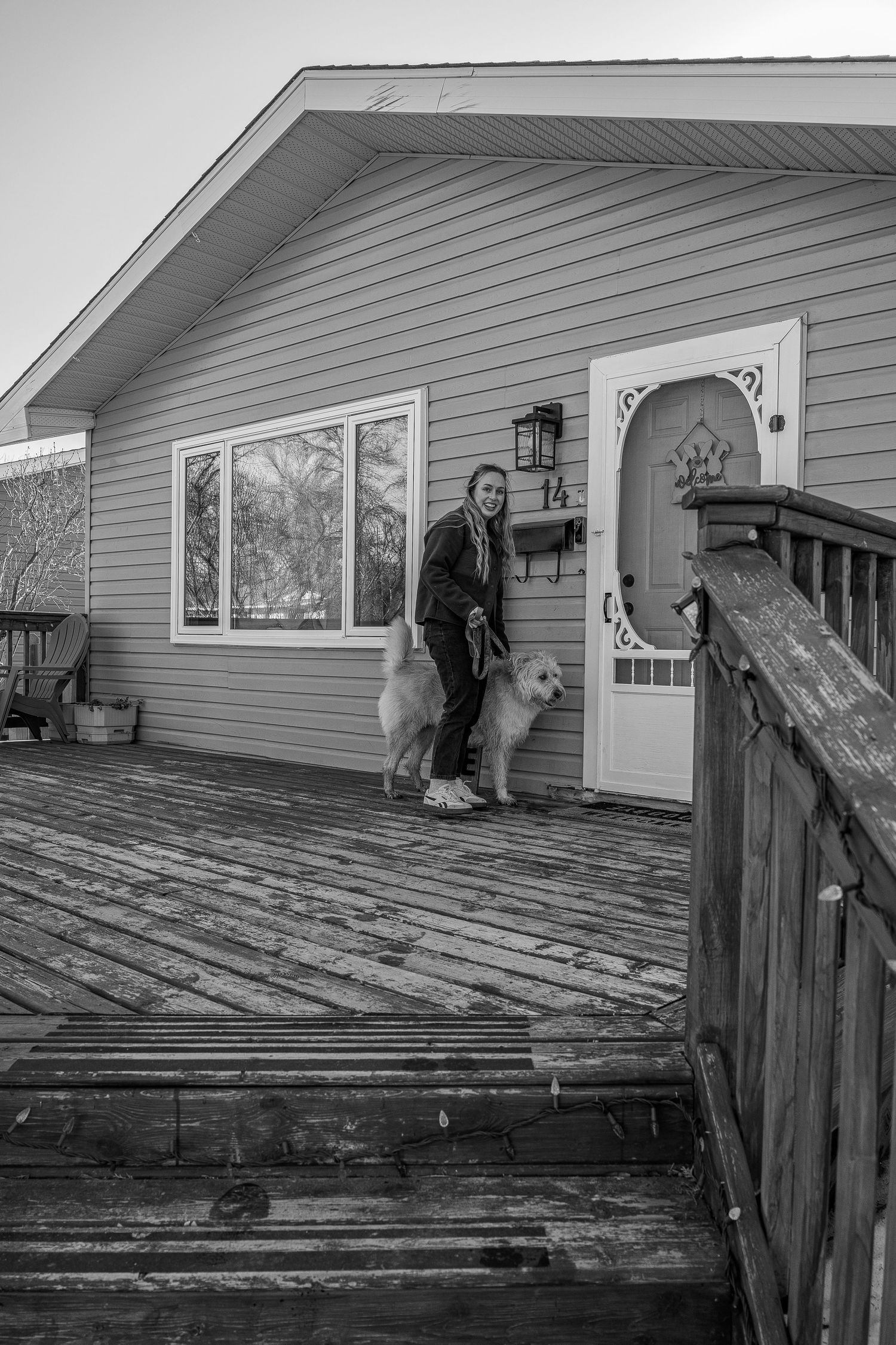 Woman stands with two white dogs on a wooden deck outside a house, black and white photo.