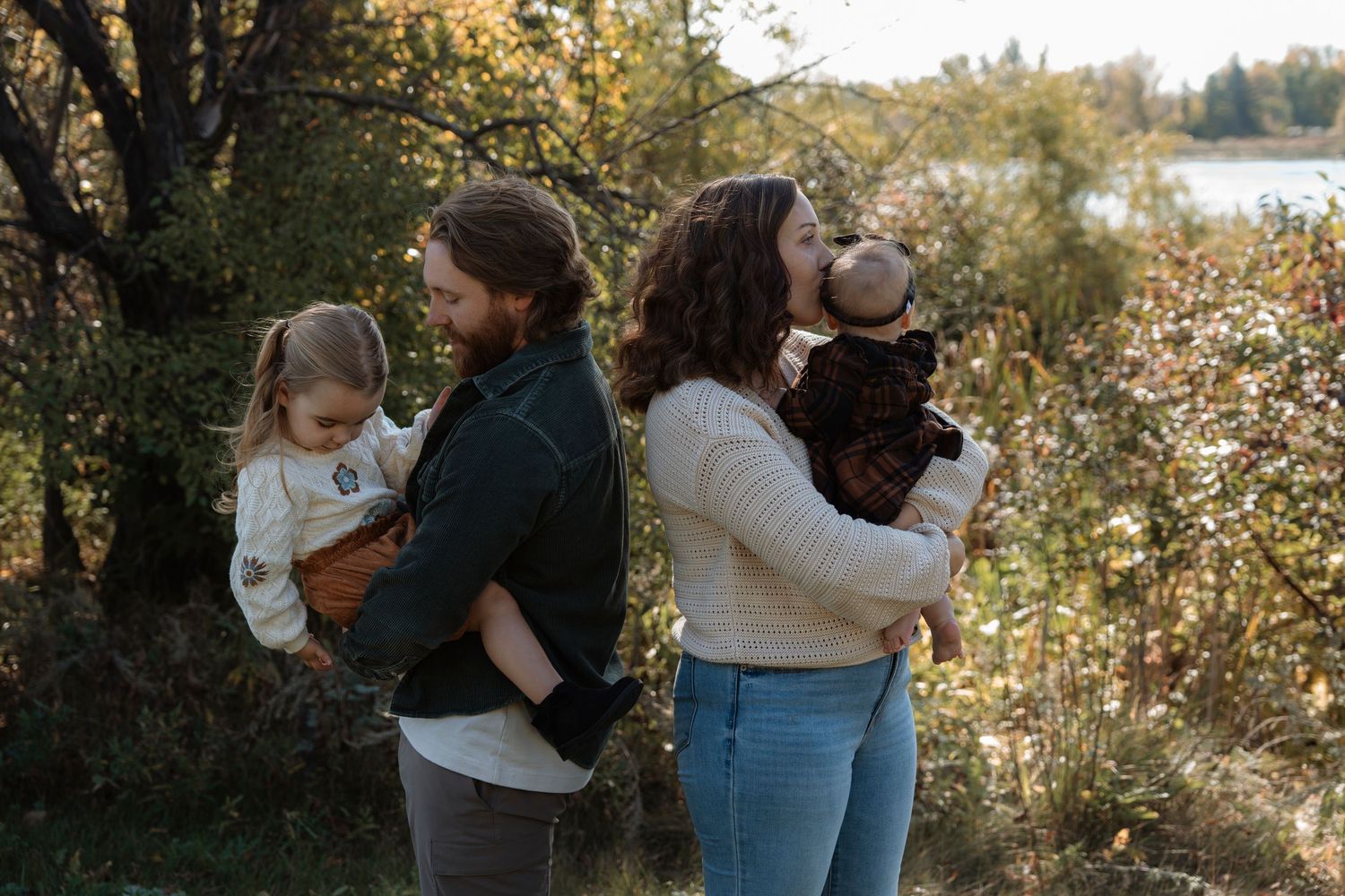 Family members share tender moments together during an outdoor autumn photoshoot by a lake at sunset.