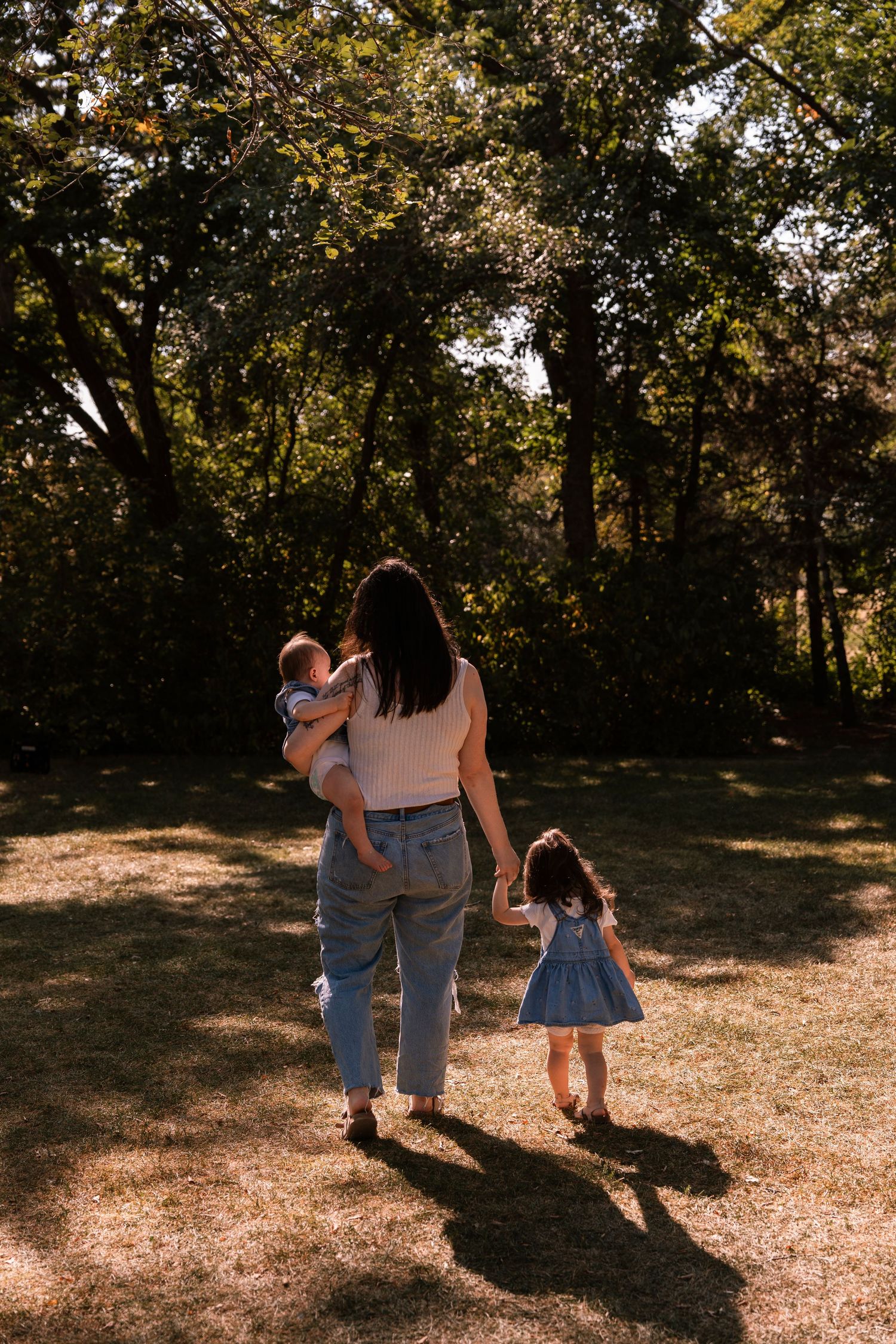 Three people walking together in a park casting long shadows during golden hour in nature. Regina Saskatchewan Family portrait photographer.